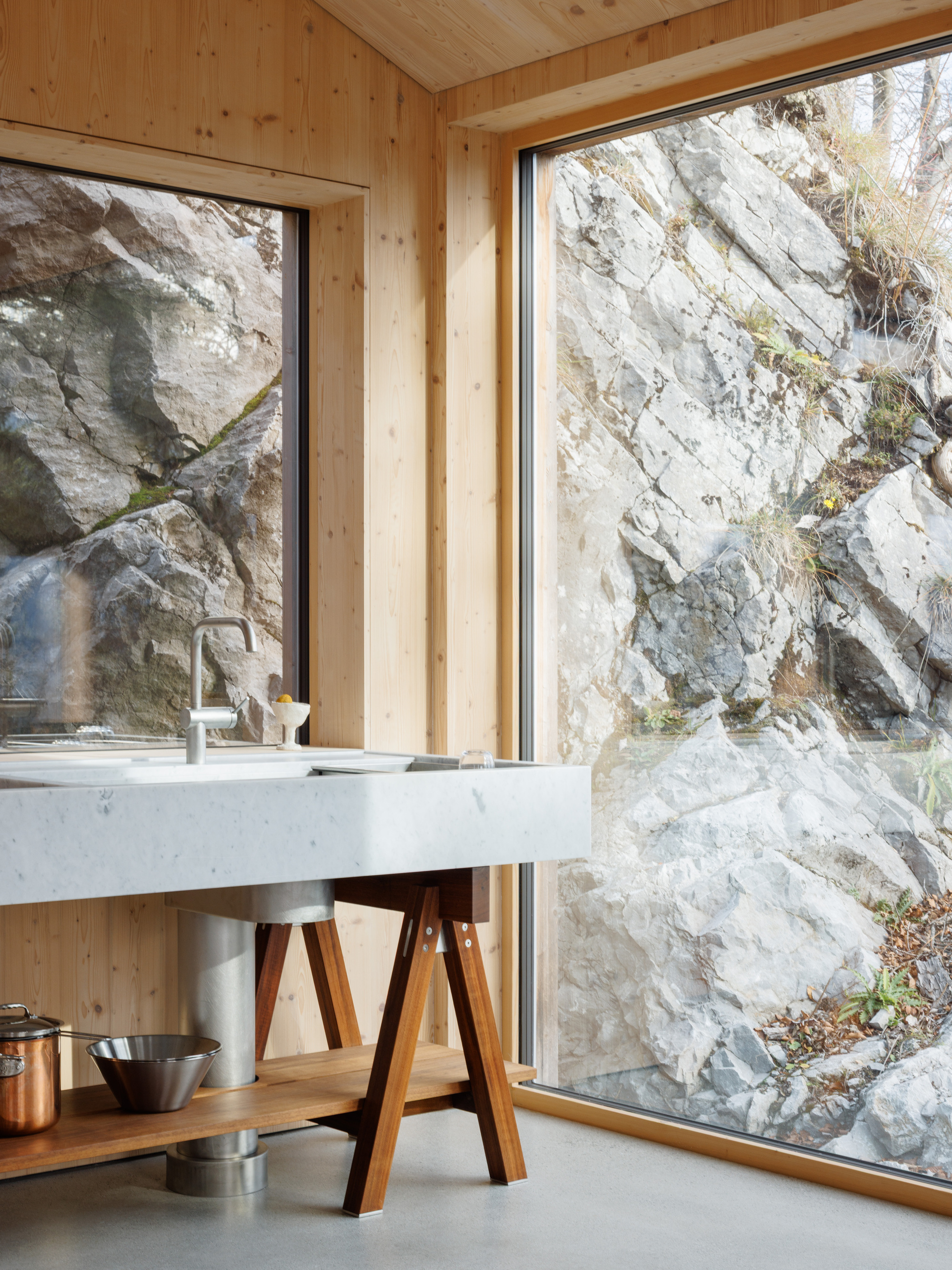 Kitchen sink on timber trestles facing floor-to-ceiling windows with exposed rock face beyond
