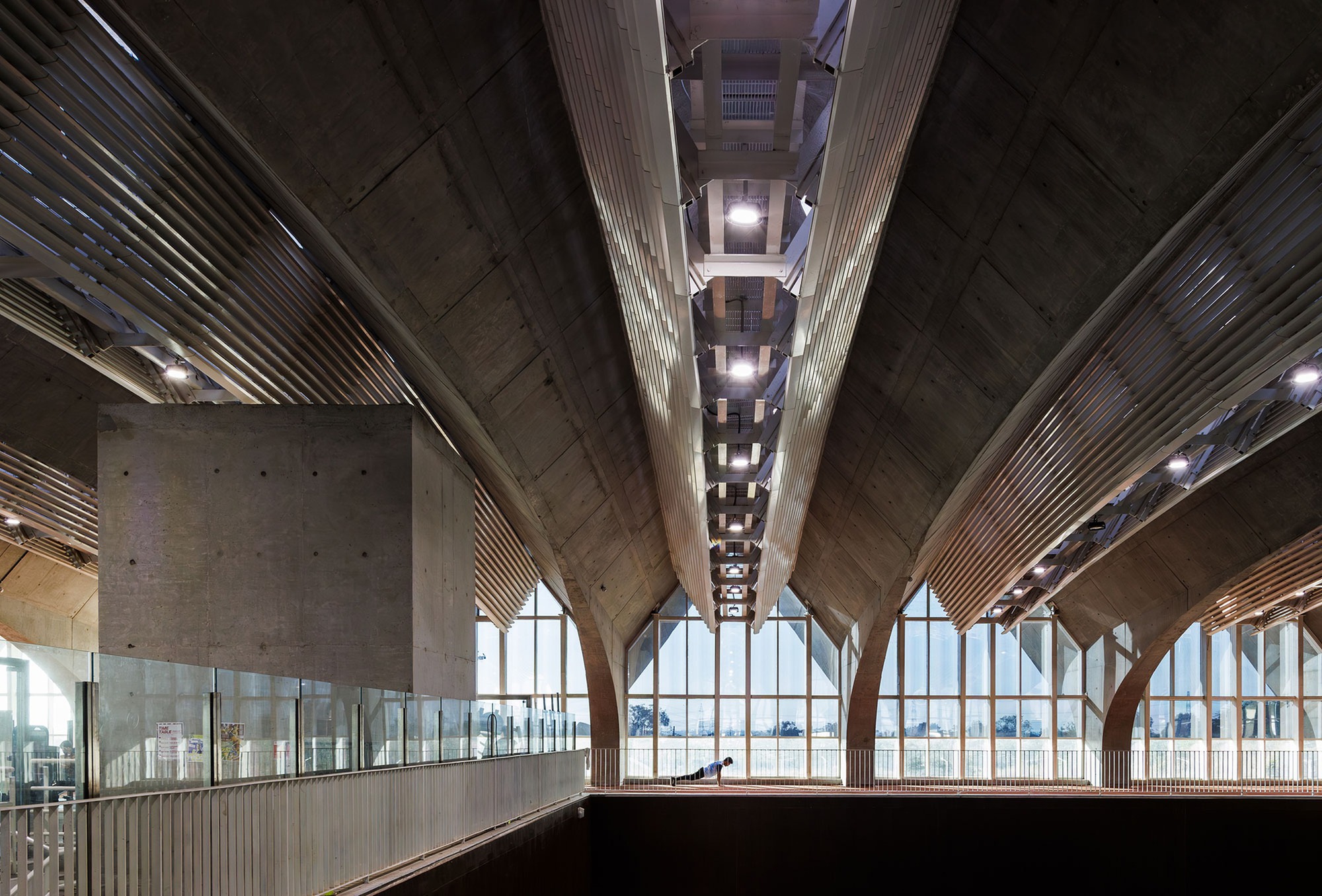 Interior view showing concrete vaulted ceiling with integrated lighting and arched glazed wall beyond mezzanine
