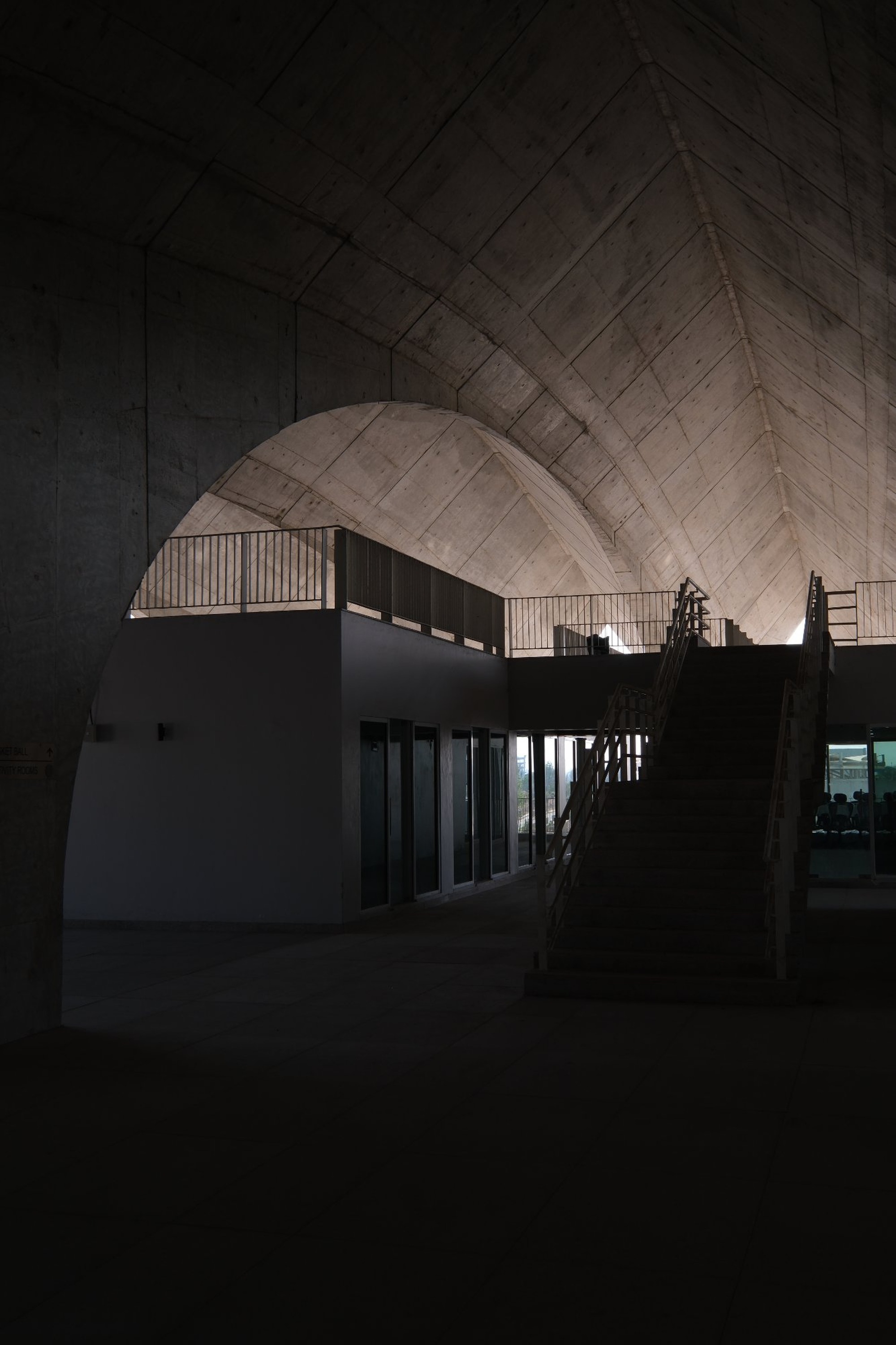 Interior view of arched concrete vault with upper-level balcony and timber screen under warm uplighting