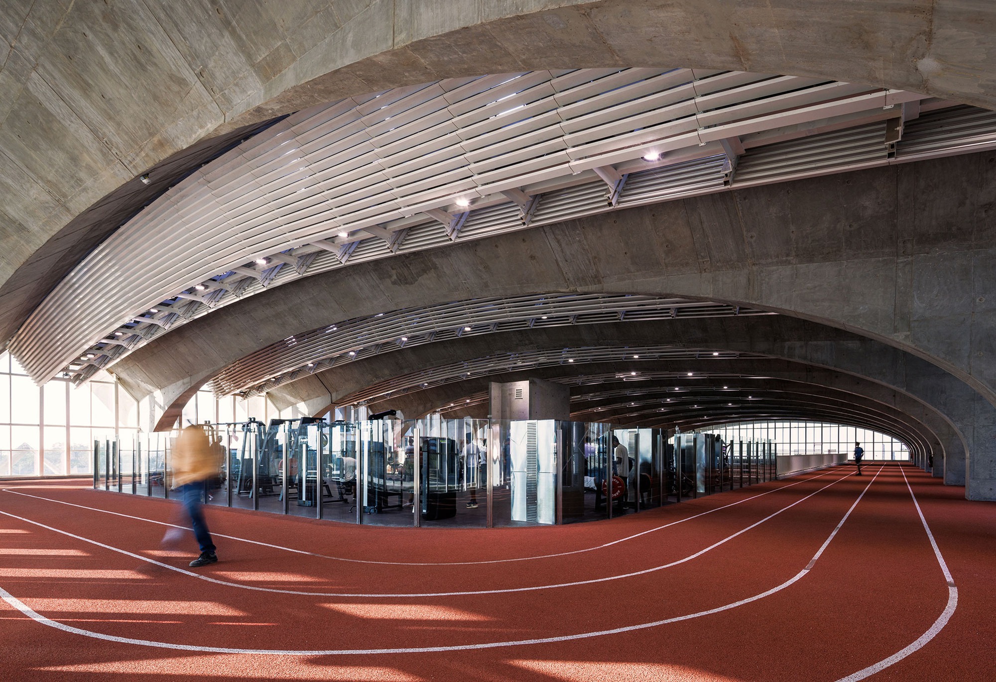 Arched vault ceiling over indoor running track with curved white lane markings and a blurred figure in motion