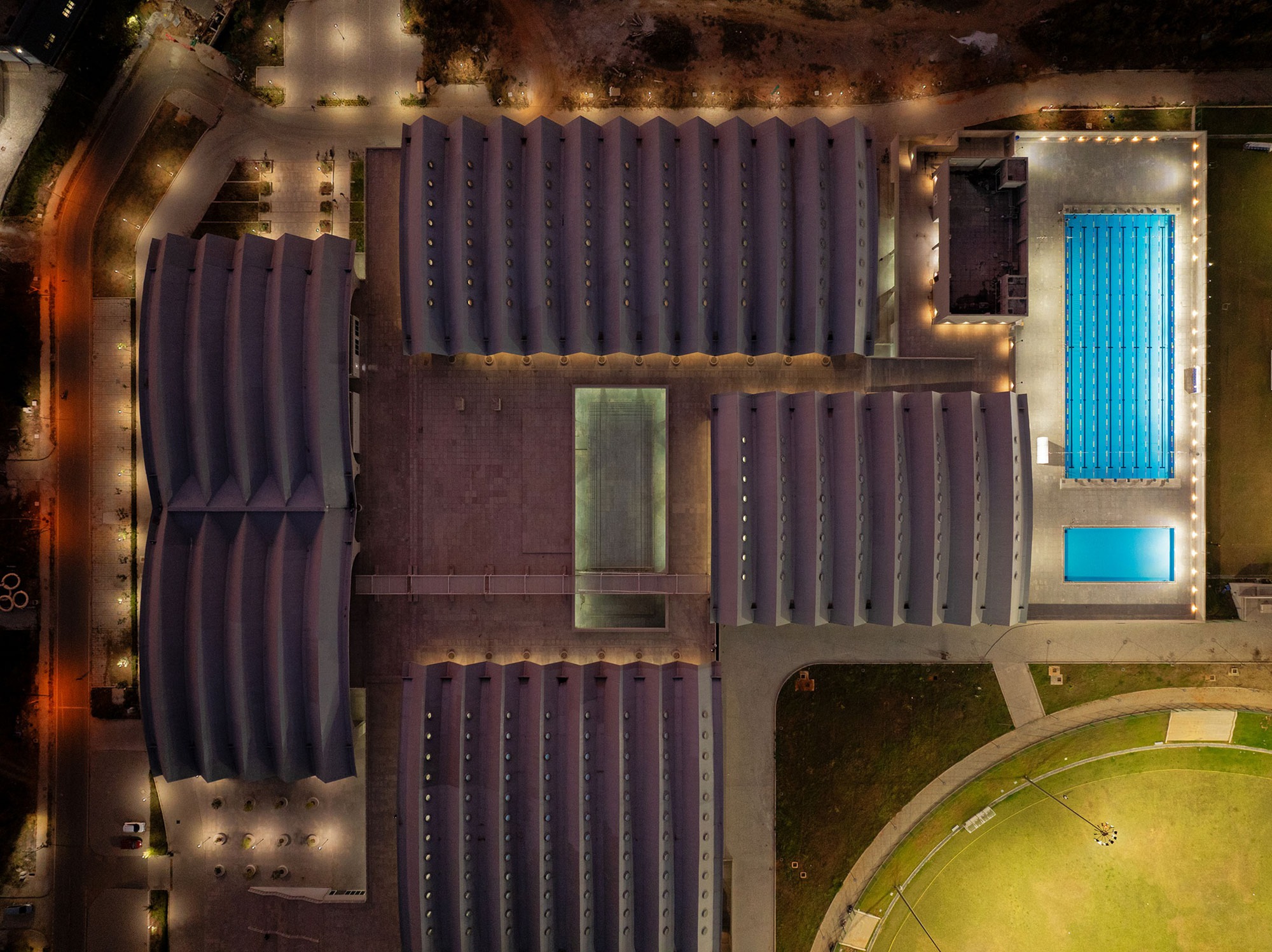 Drone view of the vaulted roofs, courtyards, and two blue pools illuminated at night