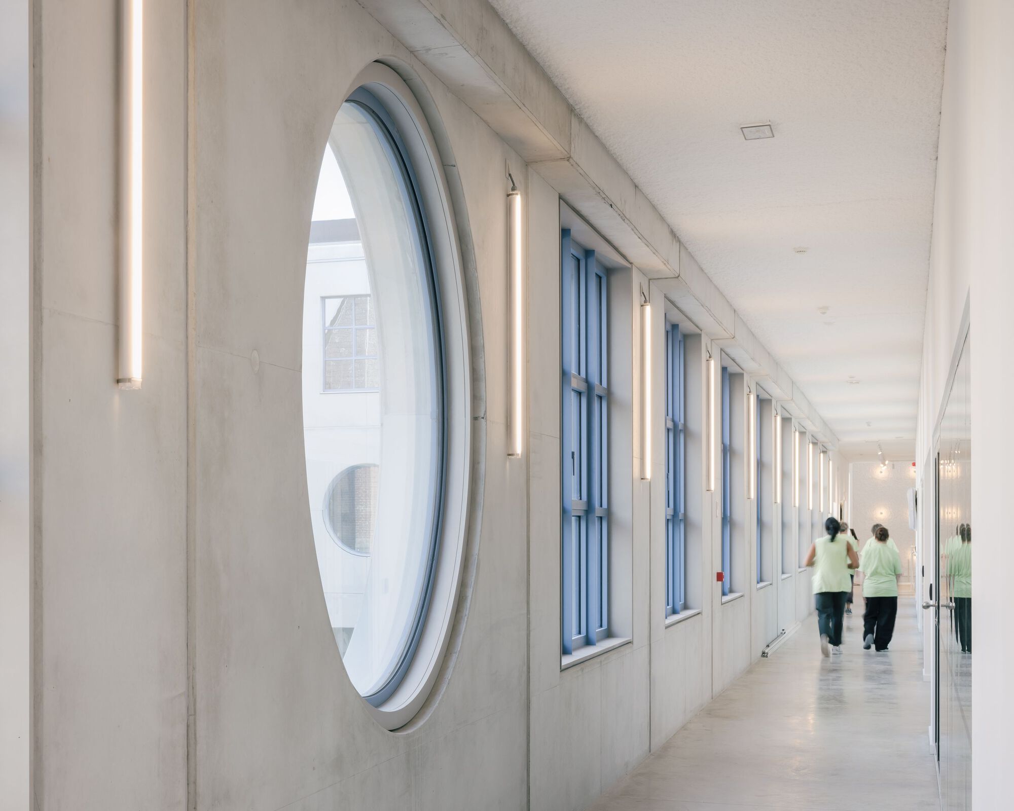 Corridor with oval window and vertical tube lights alongside two figures walking