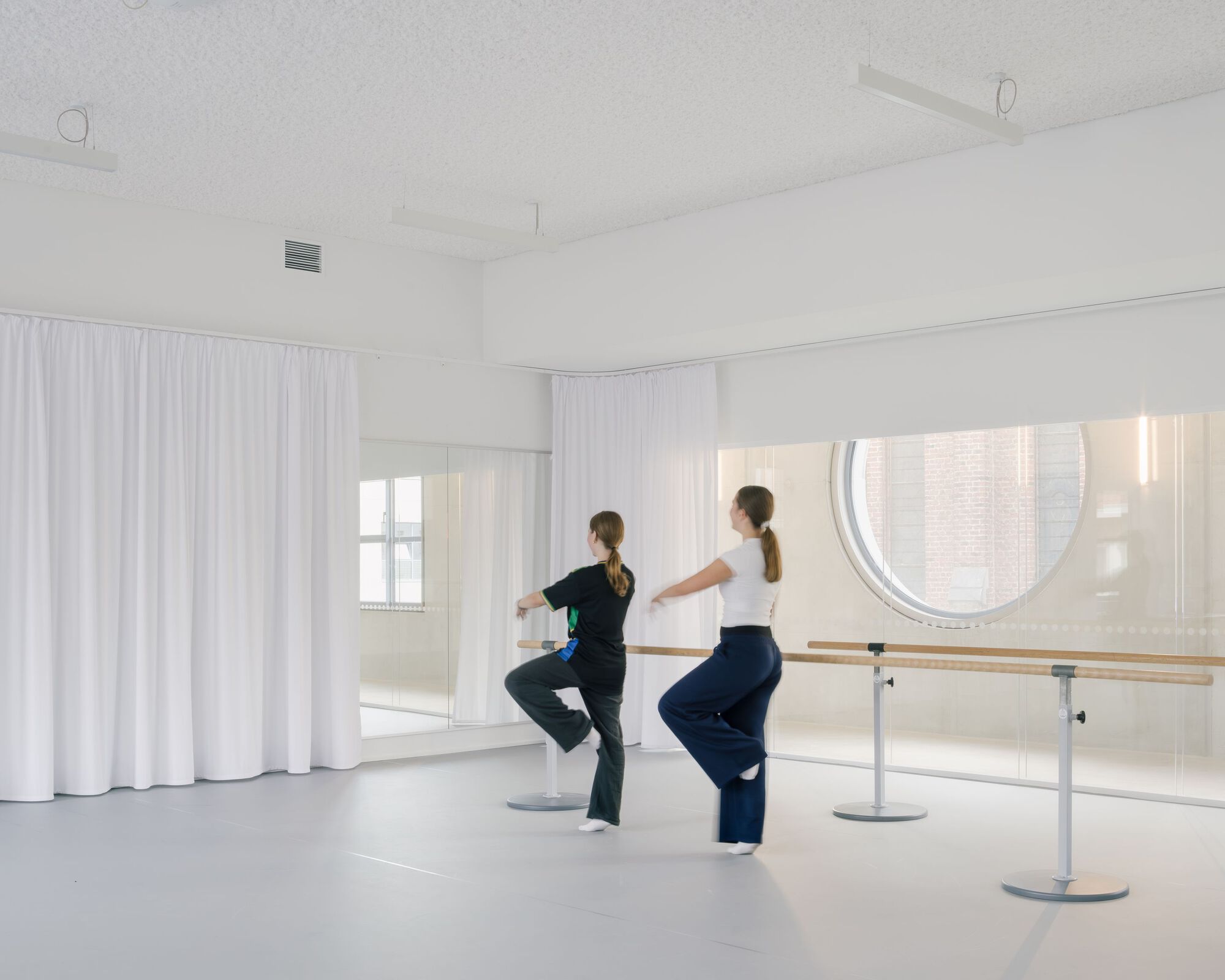 Dance studio with wooden barre and mirrored wall framing a circular window