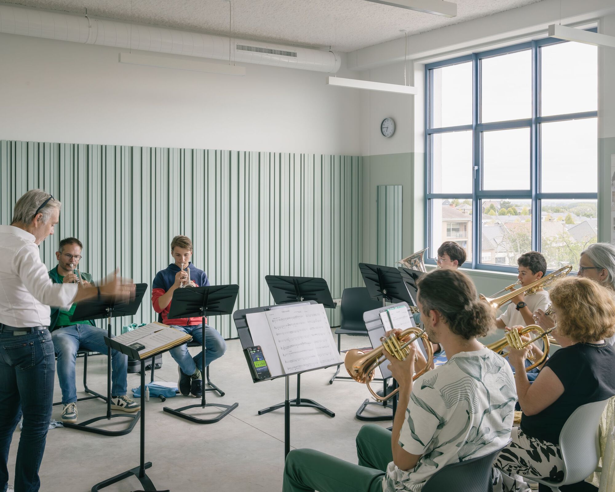 Ensemble rehearsal room with striped green wall panels and musicians seated in a circle