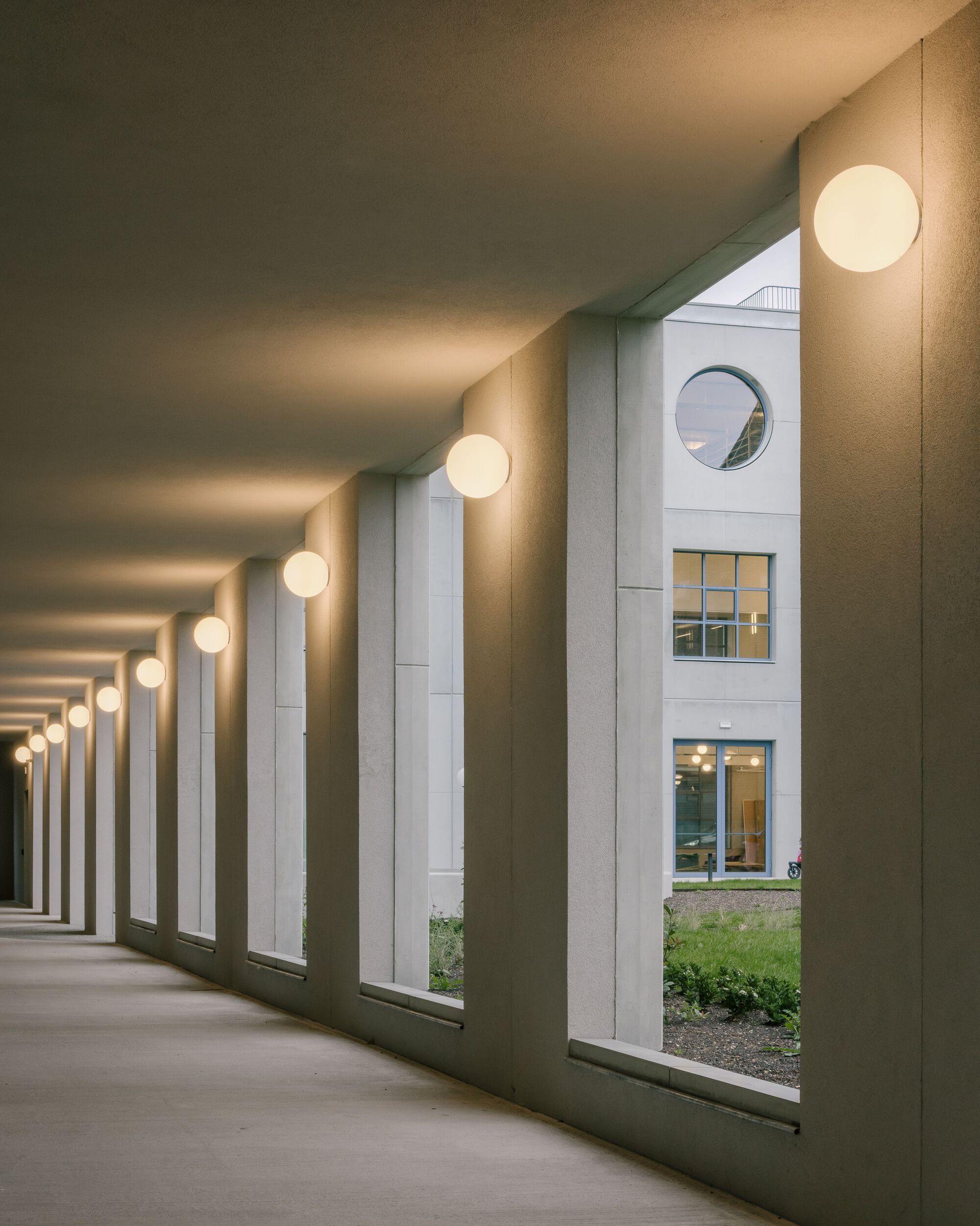 Covered colonnade with repeating concrete columns and spherical pendant lights at dusk