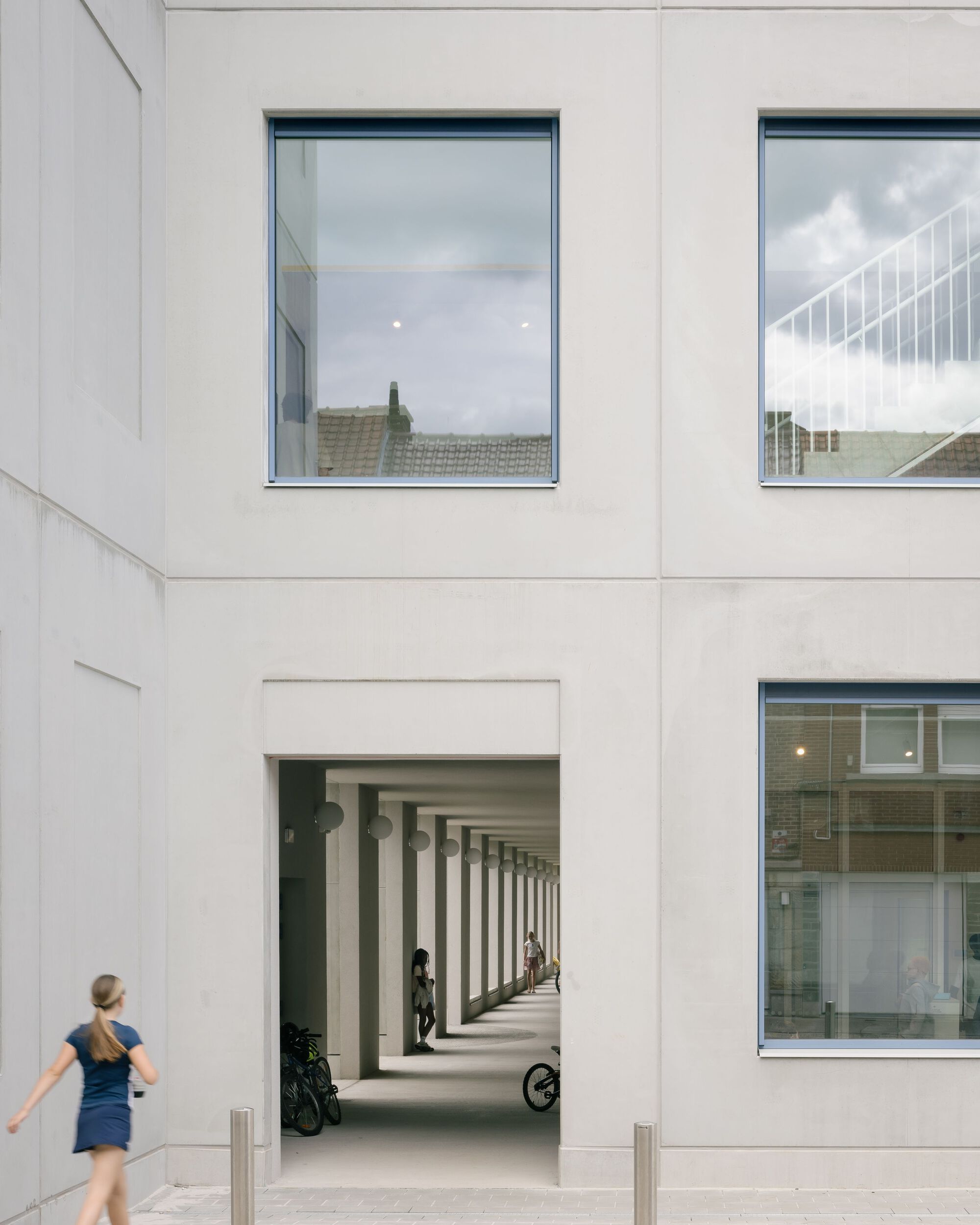 White facade opening framing the colonnade with a woman walking past in afternoon light