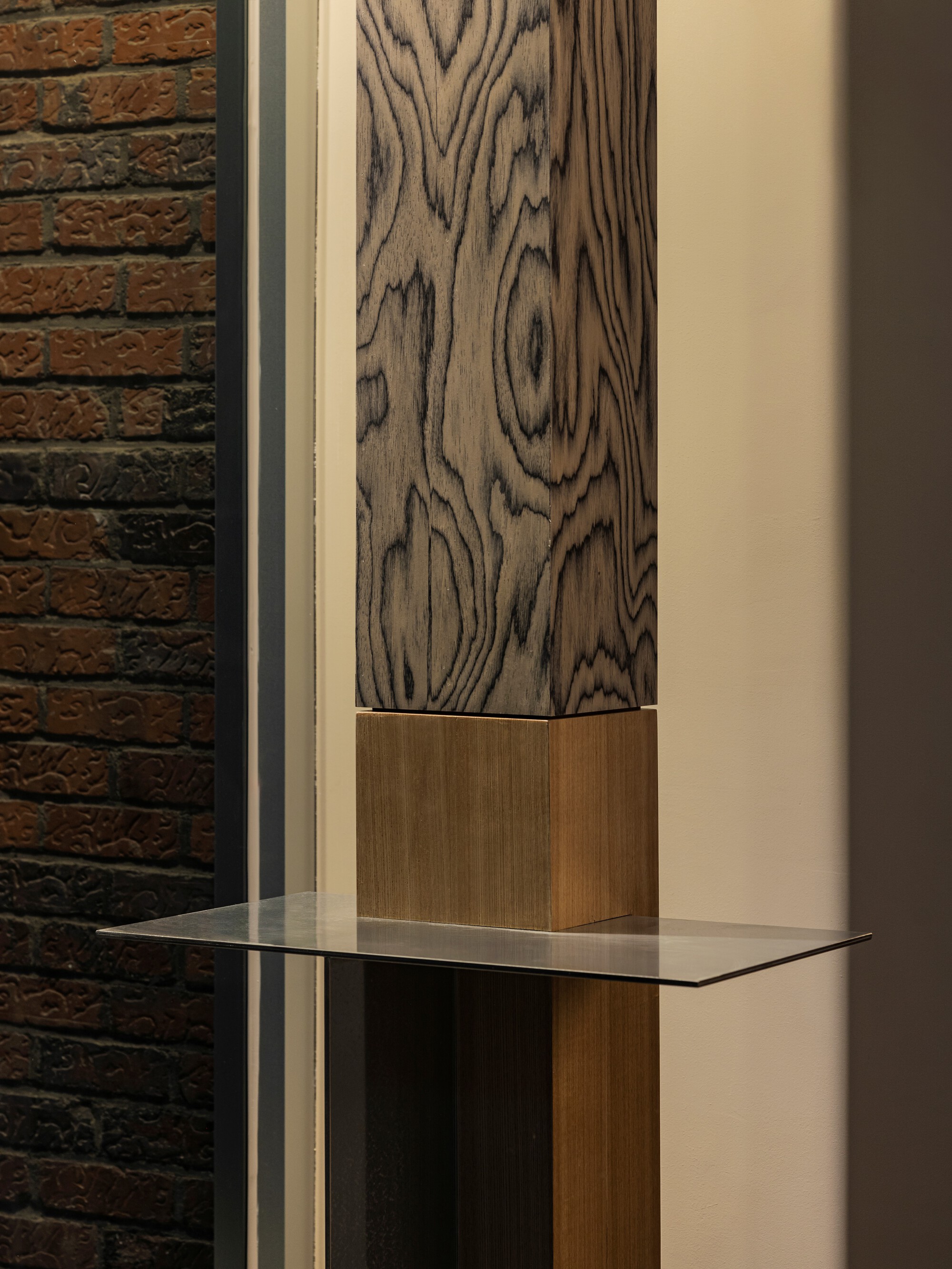 Detail of wood-grained column with glass shelf against exposed brick wall