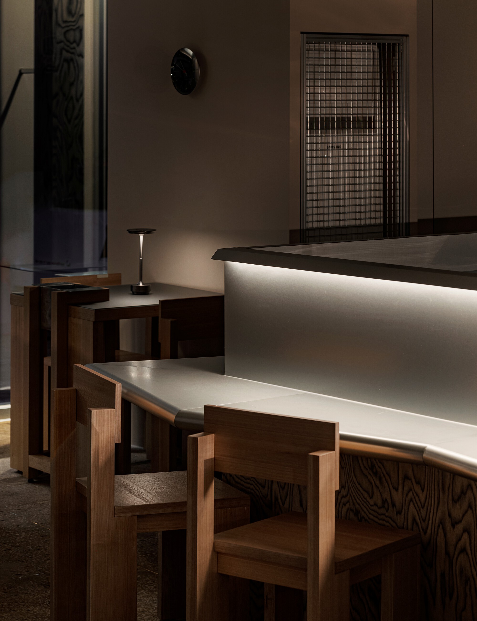 Oak seating adjacent to backlit counter with wire mesh screen in the background