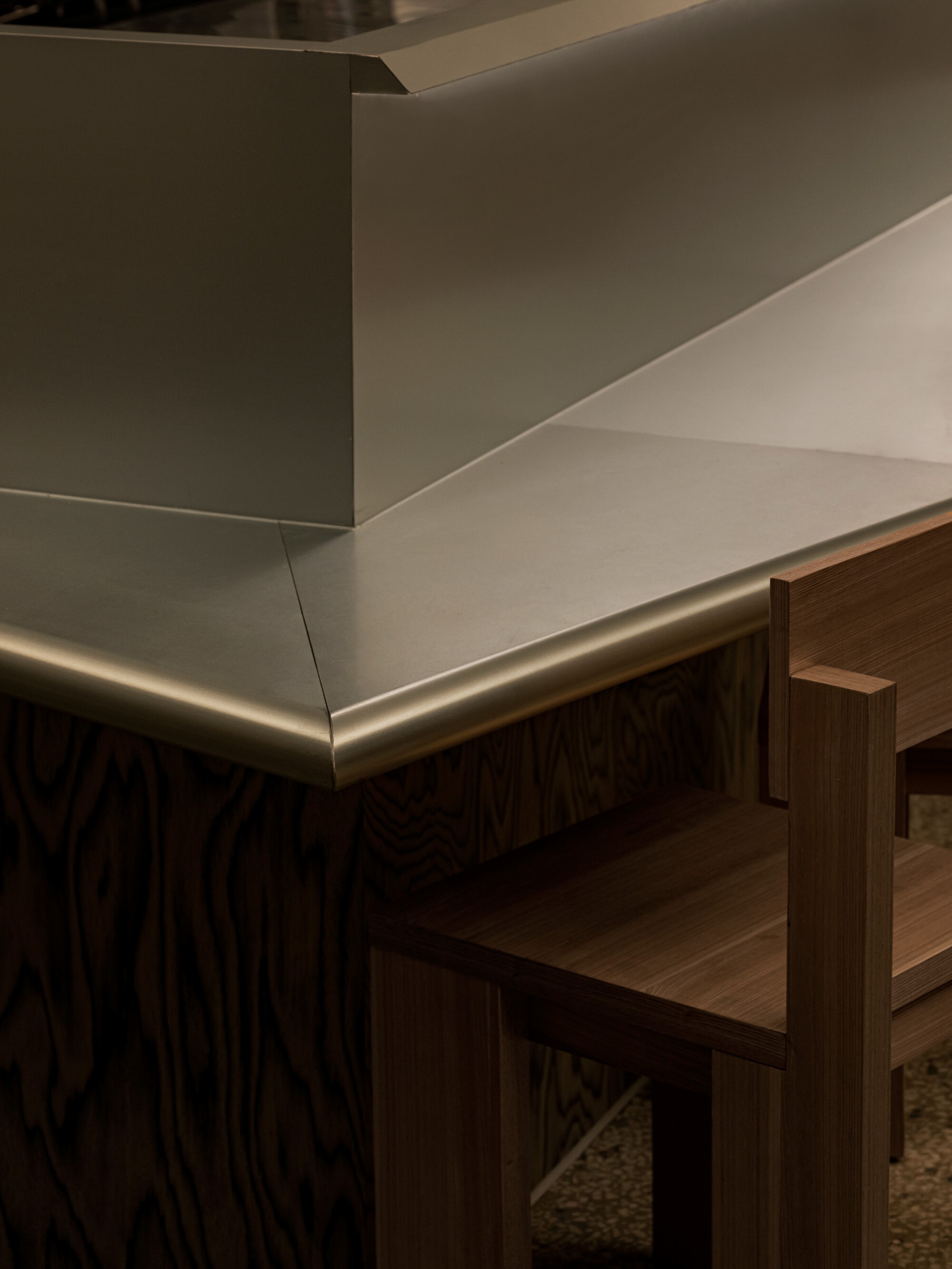 Detail of brushed brass counter edge meeting timber millwork beneath white plaster walls