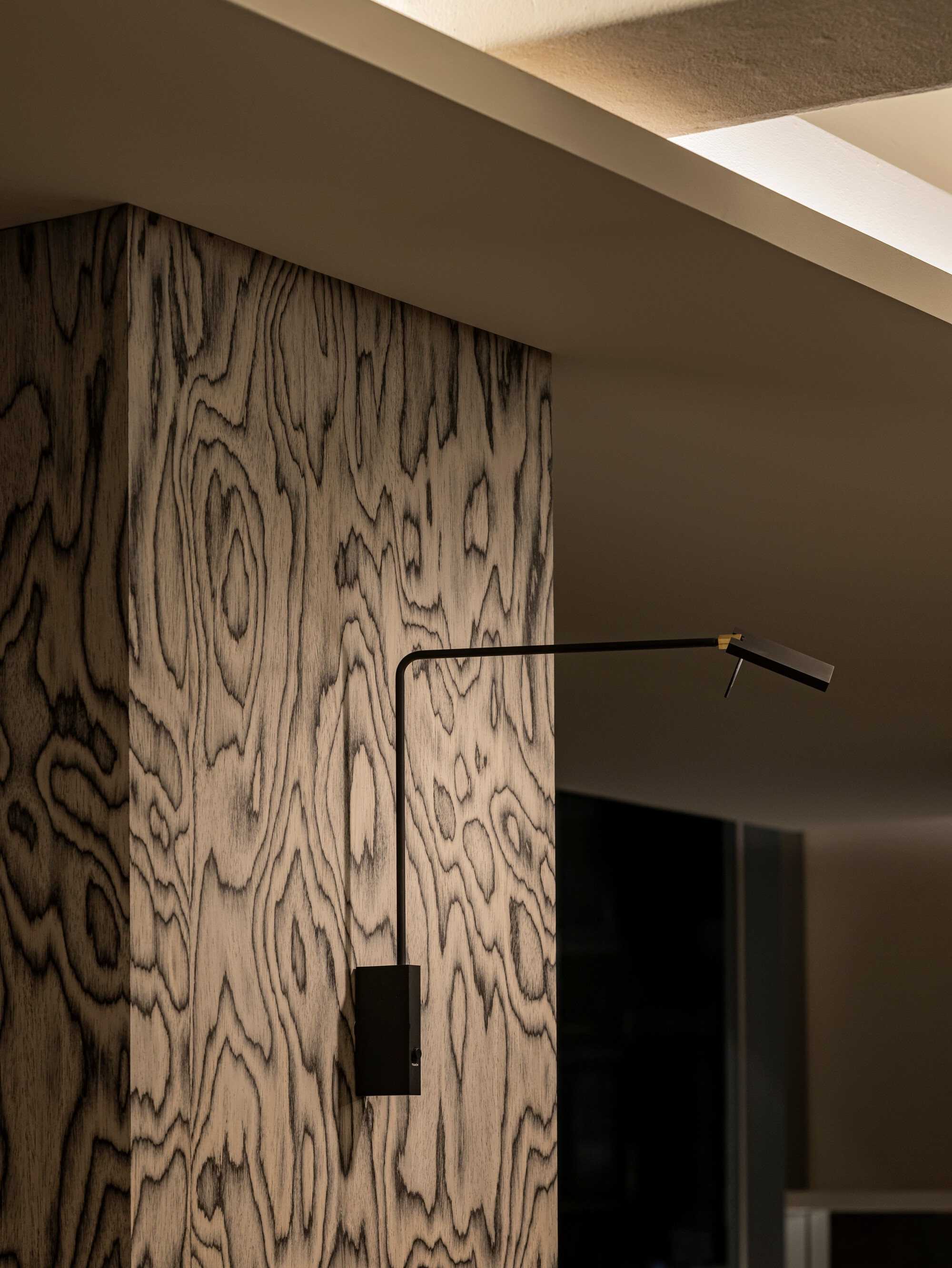 Figured wood grain wall panel with black swing-arm wall sconce in recessed ceiling