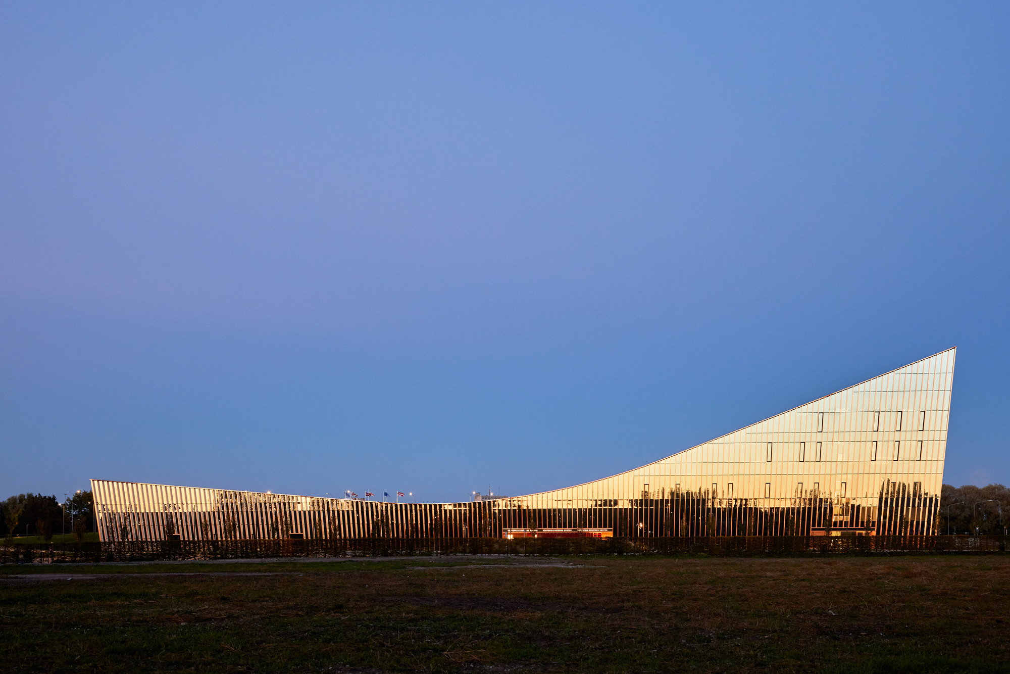 Long elevation of the illuminated vertical fin facade and angled glass volume at twilight