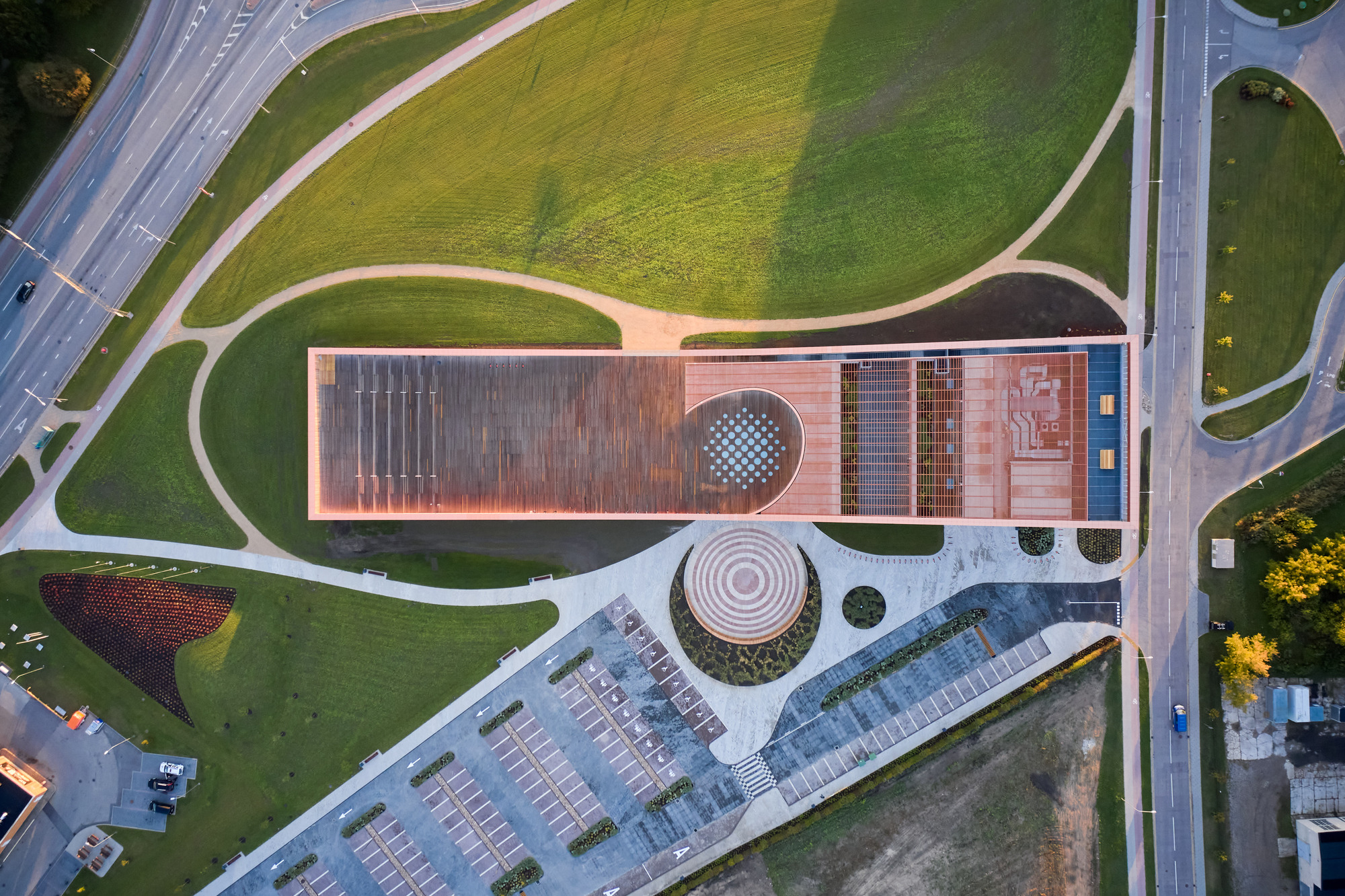 Aerial view of the copper-clad roof with circular skylights surrounded by curving pathways and adjacent parking lot