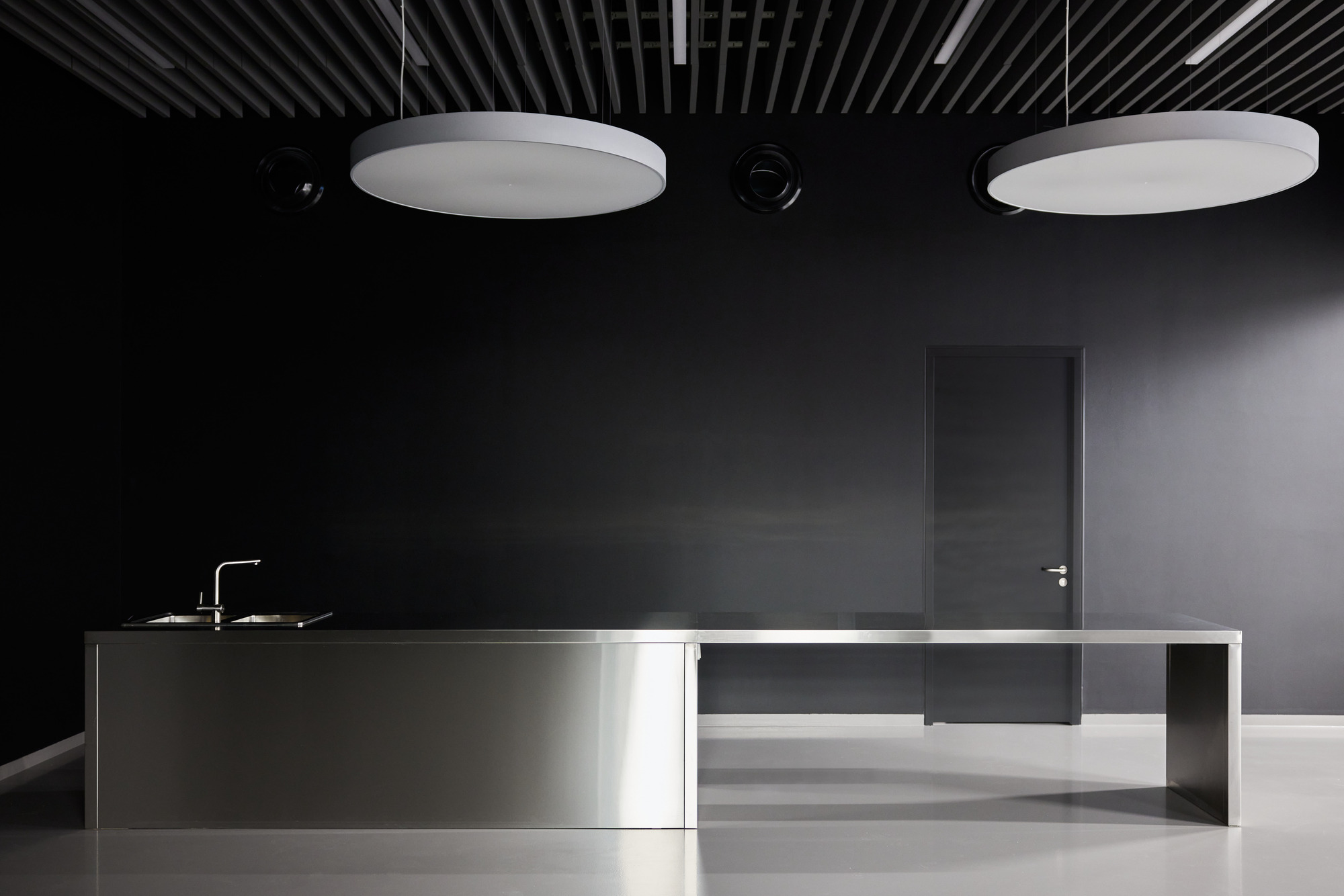 Minimalist kitchen island with stainless steel base and integrated sink beneath two circular ceiling fixtures