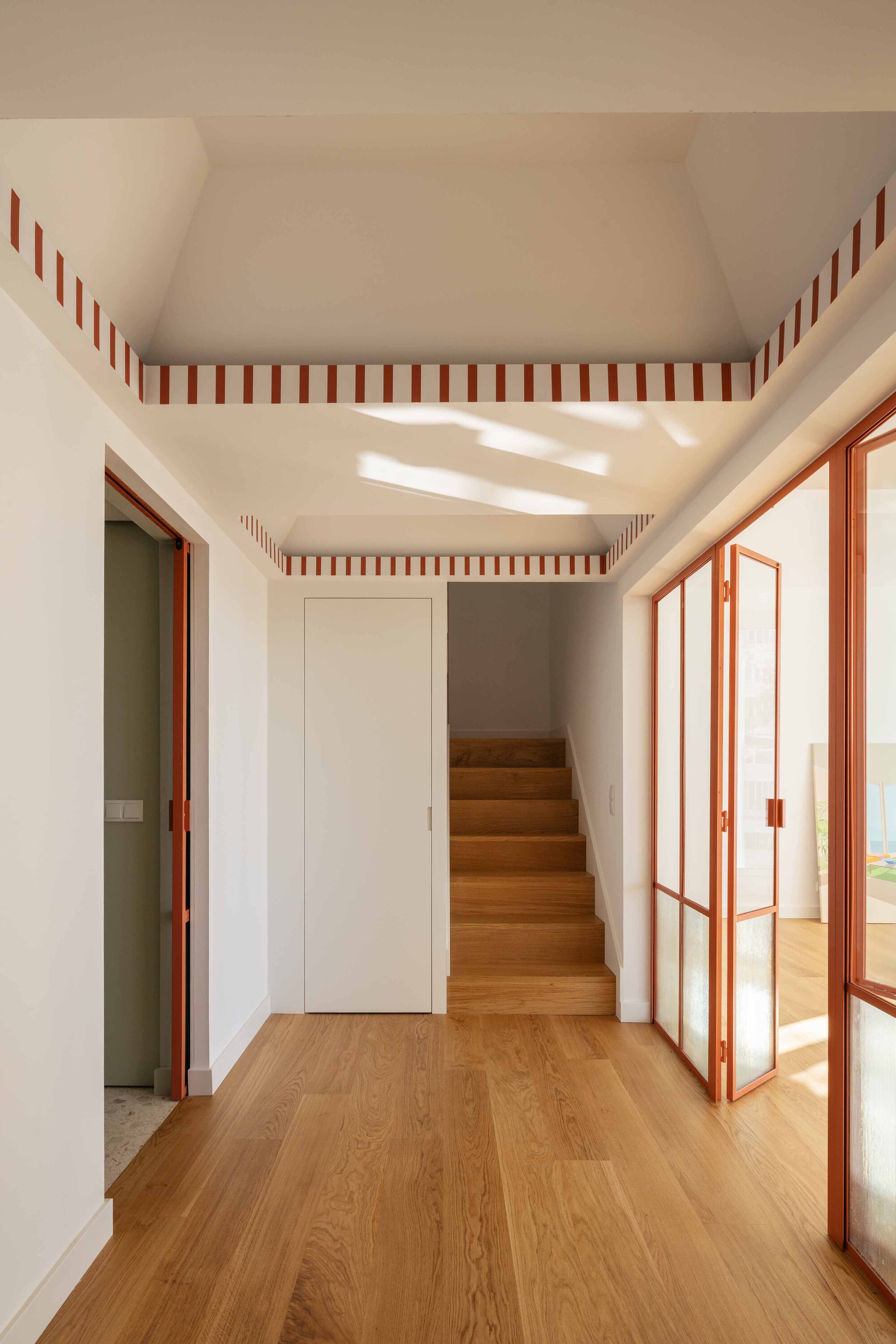 Hallway with timber staircase and striped ceiling detail lit by overhead skylight