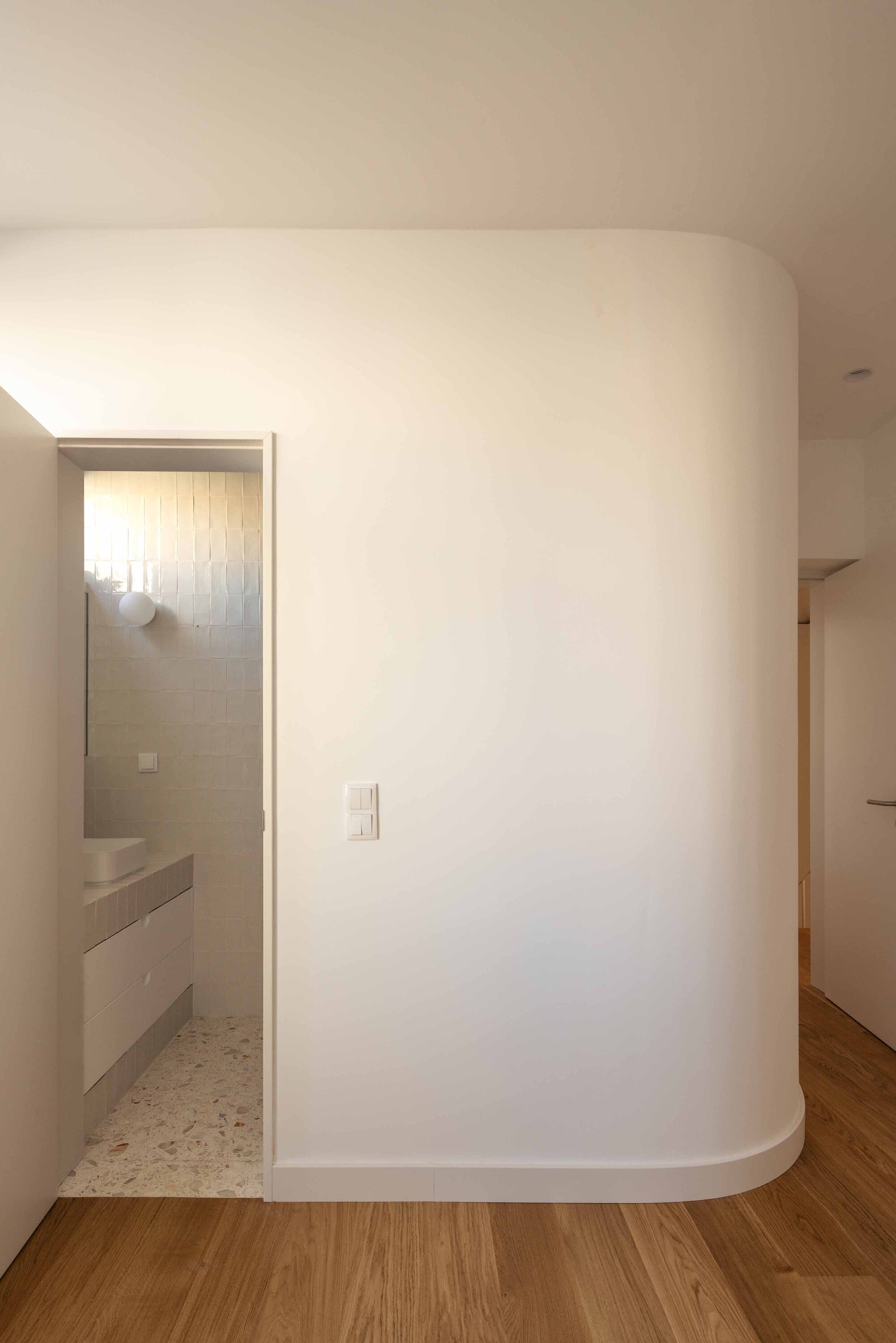 Curved white partition wall with doorway opening to tiled bathroom beyond