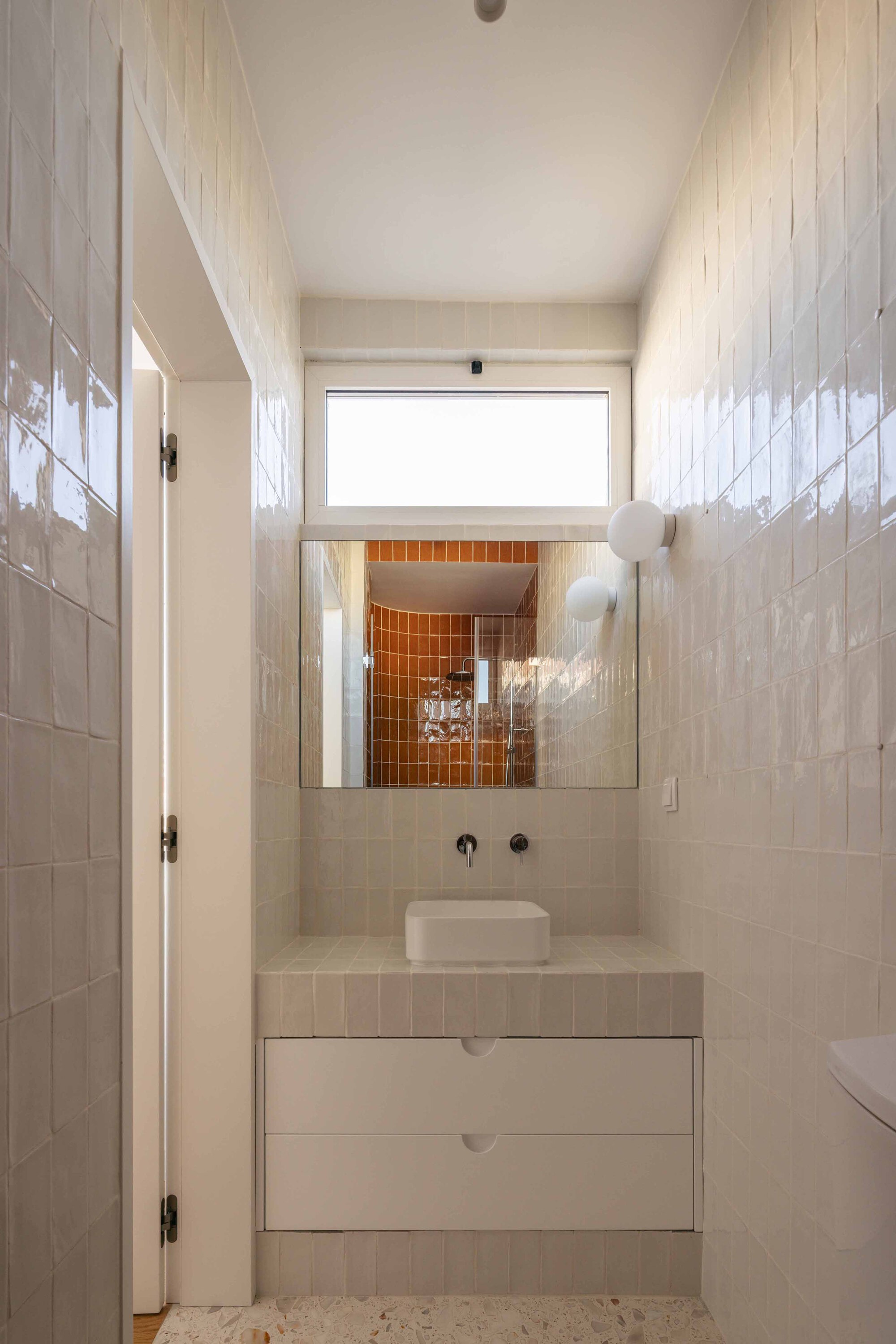 Bathroom vanity with white tile walls and mirror reflecting orange tiled shower niche