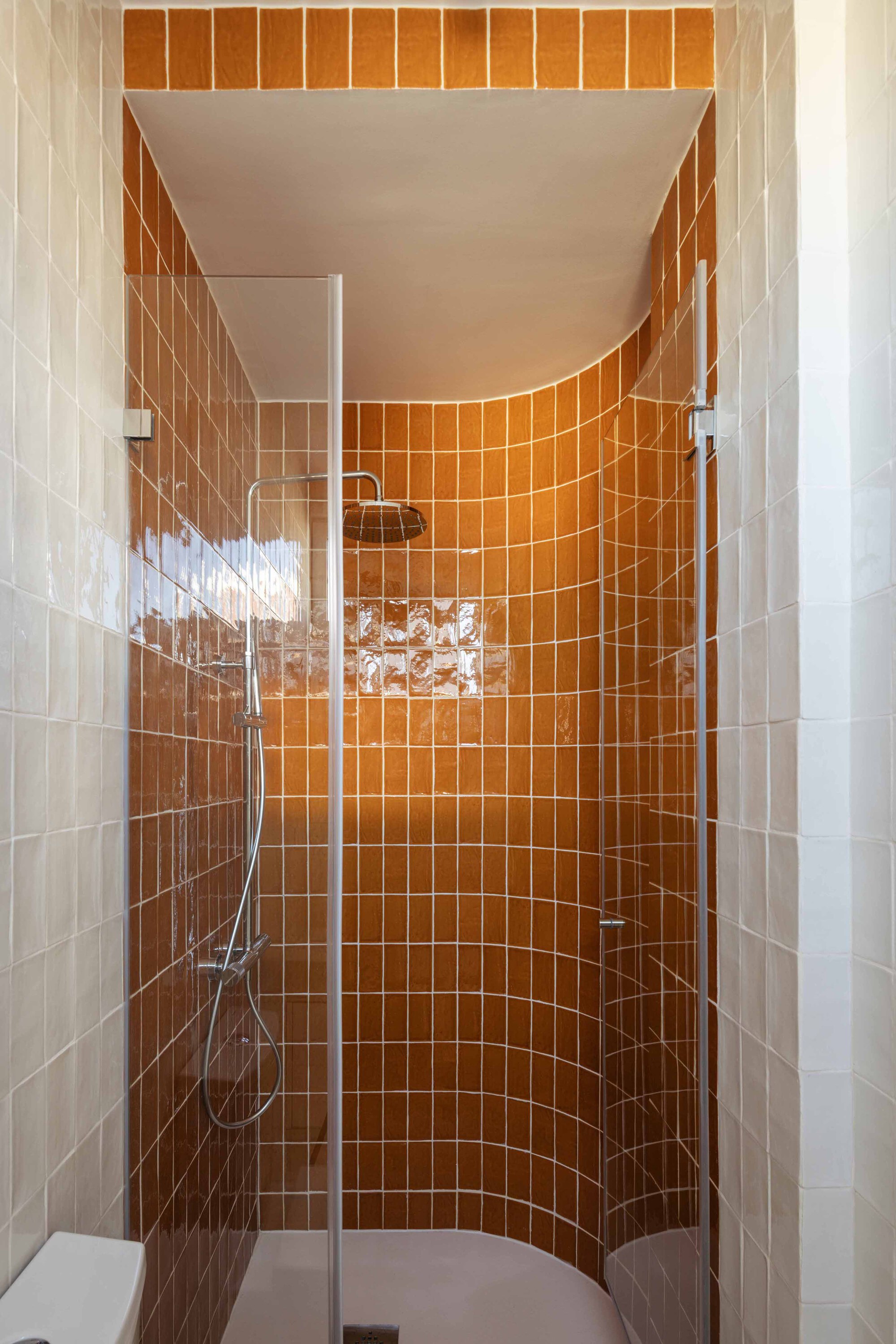 Curved shower stall lined with orange square tiles and fitted with chrome fixtures