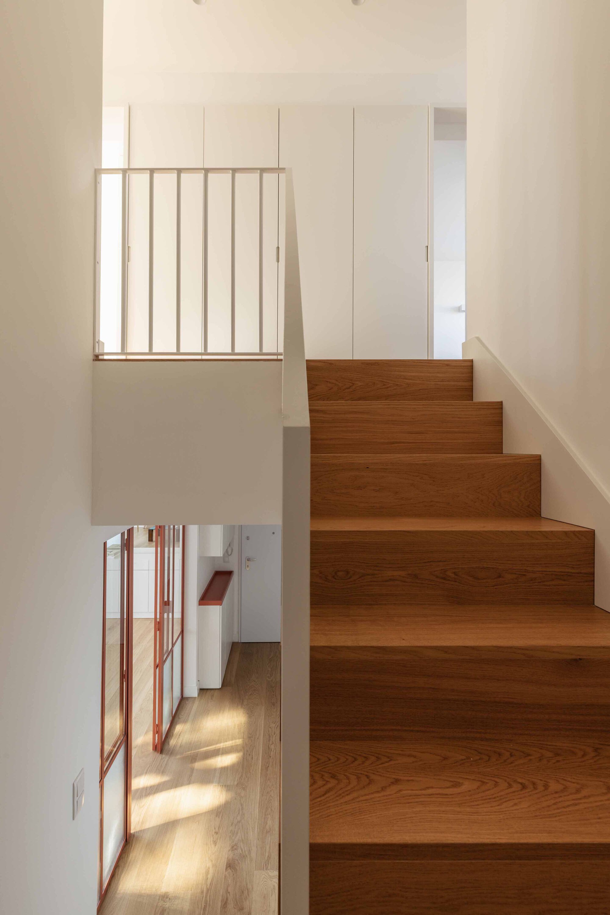 Timber staircase with vertical balustrade overlooking hallway with sunlight streaming through windows