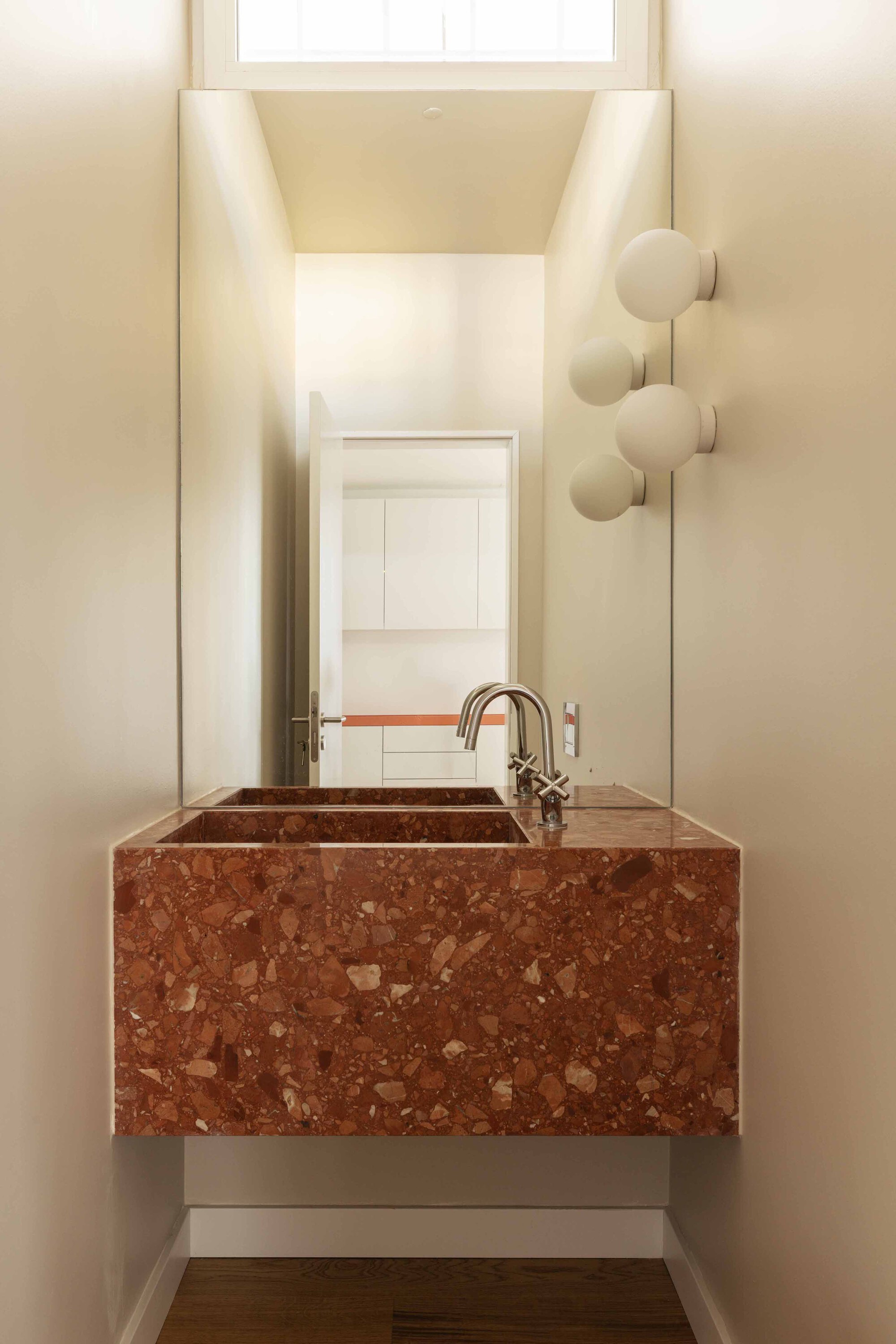 Red terrazzo basin with integrated counter and polished brass faucet in a narrow powder room