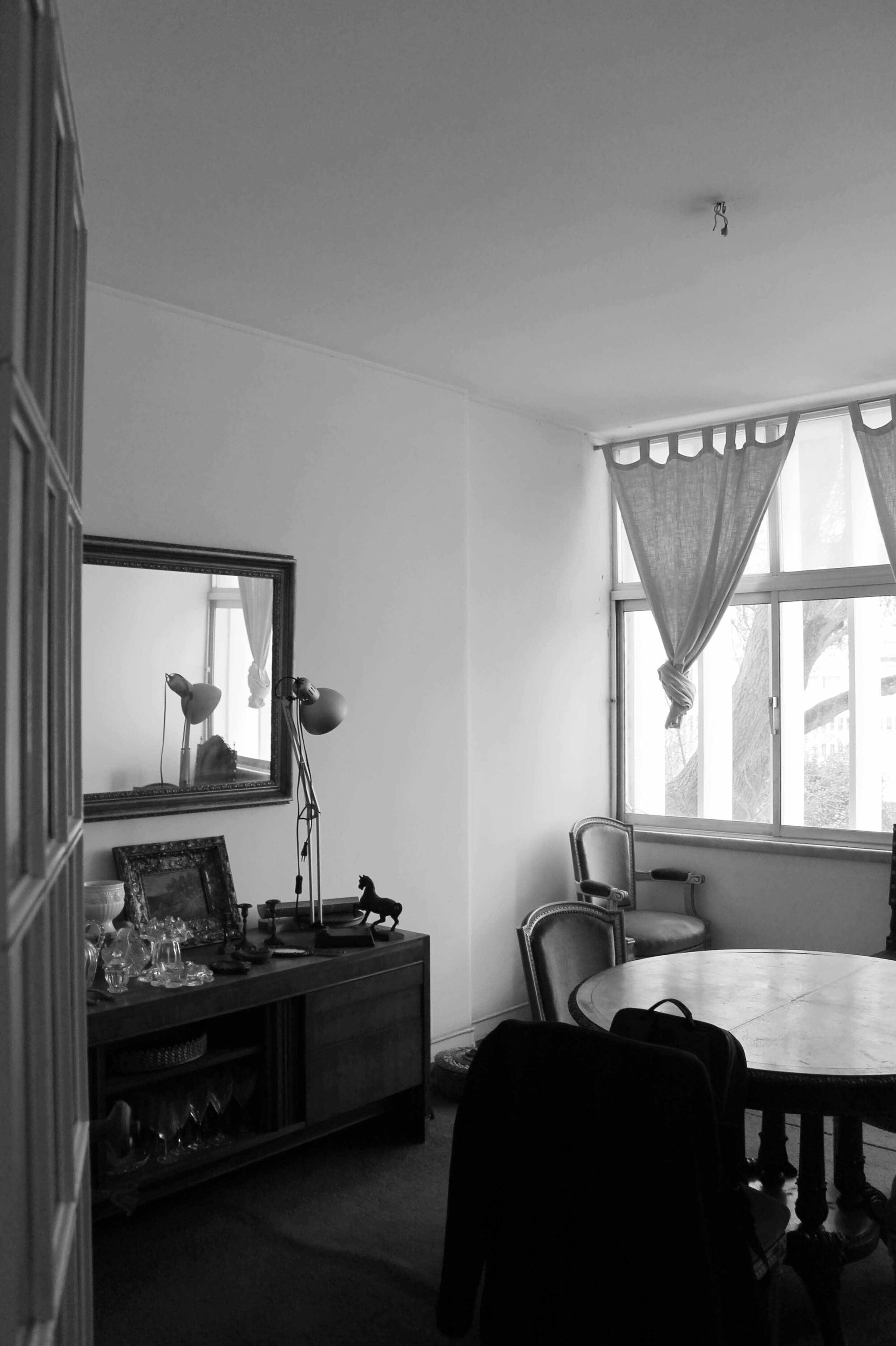 Black and white photograph of a dining room with curtained window and sideboard