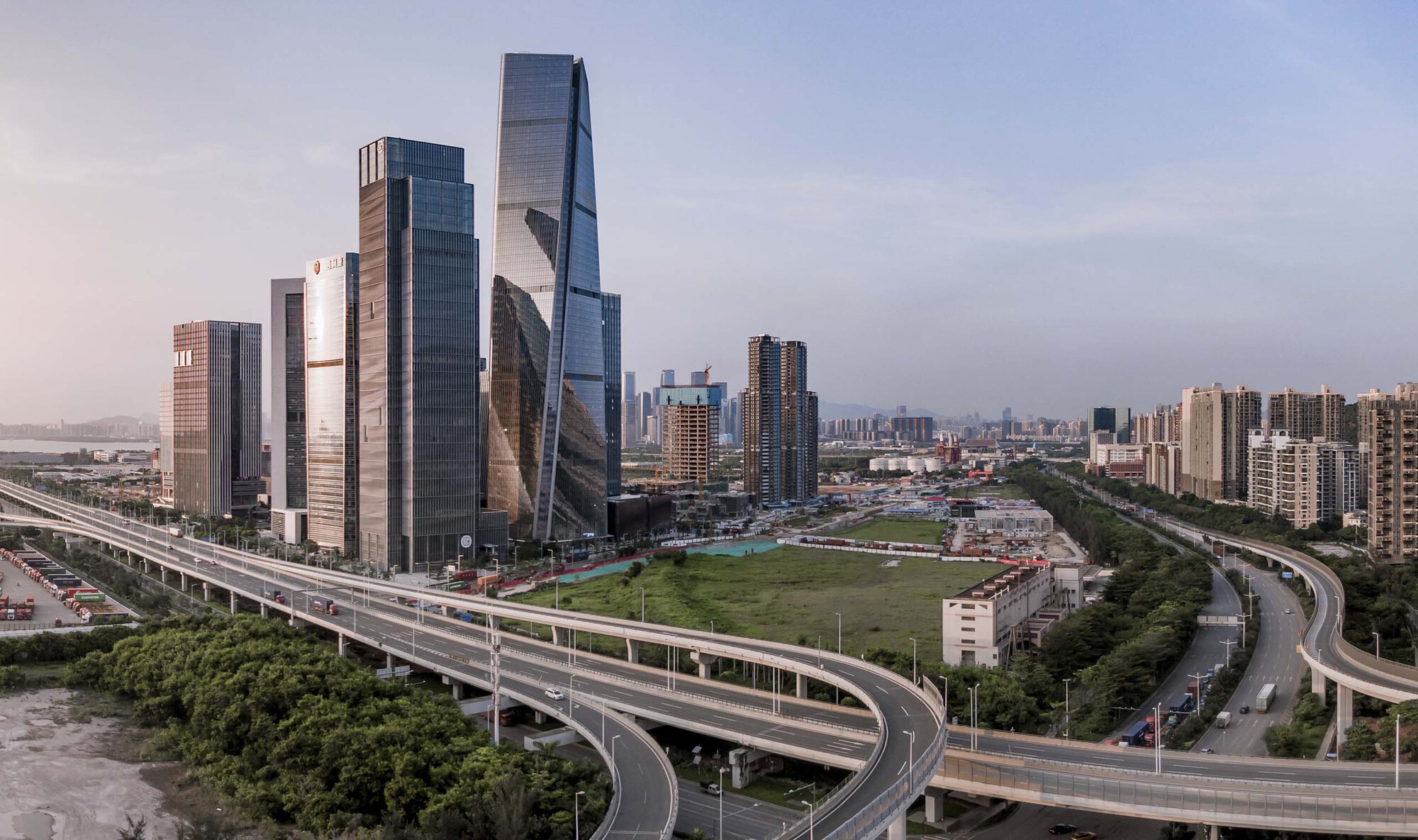 Cluster of glass towers framed by elevated highway ramps and green parkland at dusk