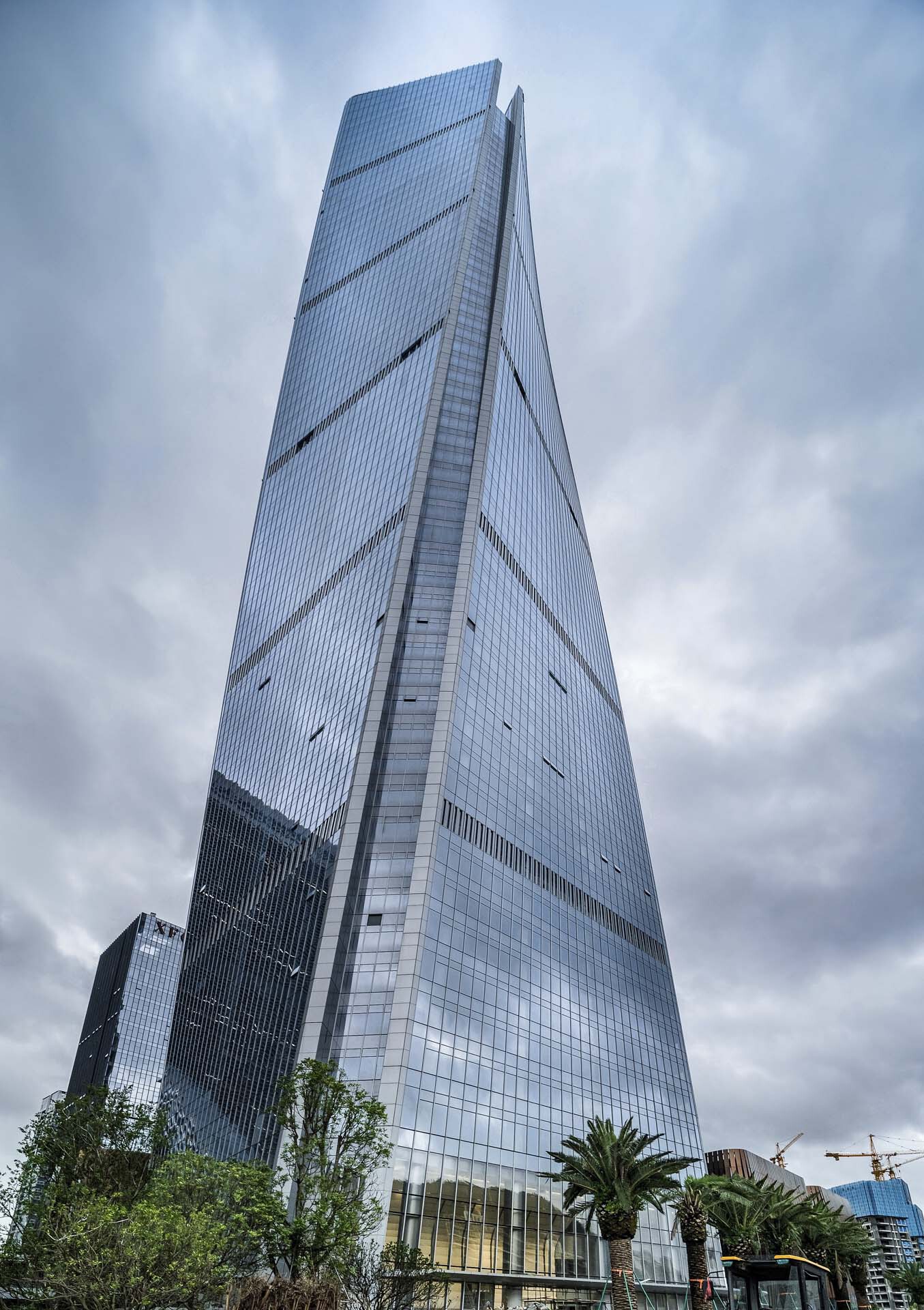 Full height view of the tapered glass tower with diagonal bracing lines under overcast sky