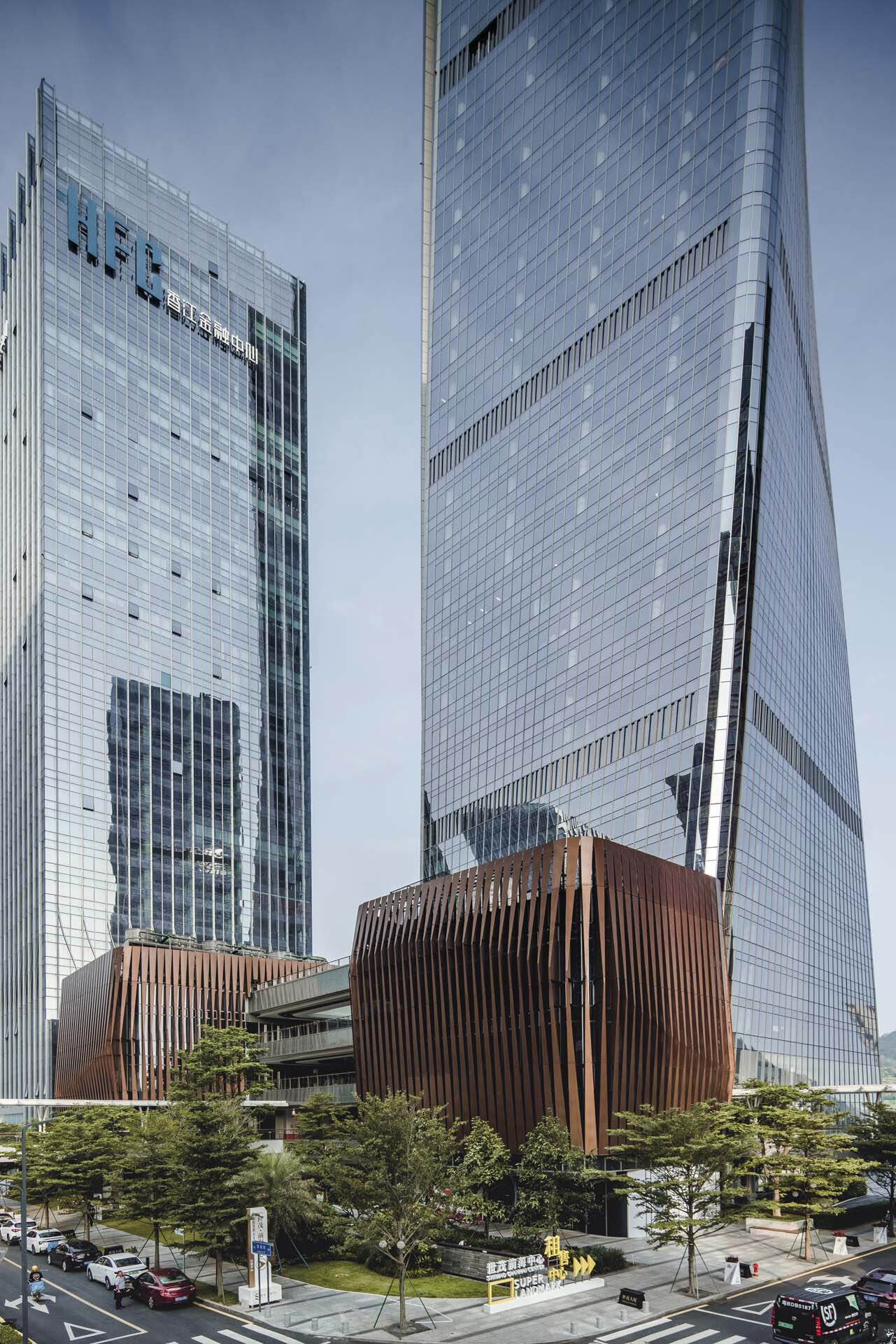 Curved bronze louvered pavilion at the base of the glass tower surrounded by planted evergreens