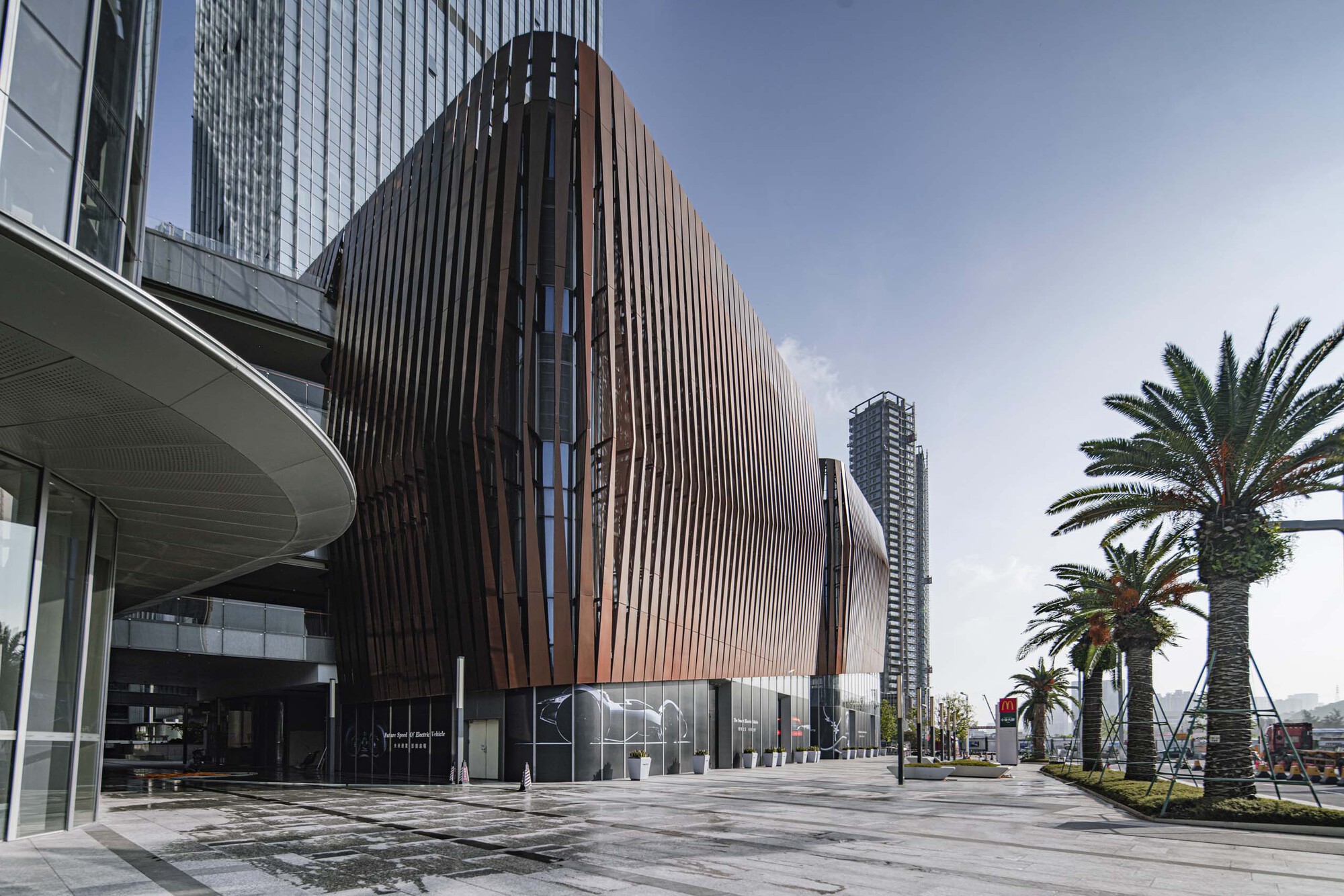 Side view of the rippling metal-clad volume beside a covered walkway and rows of palm trees