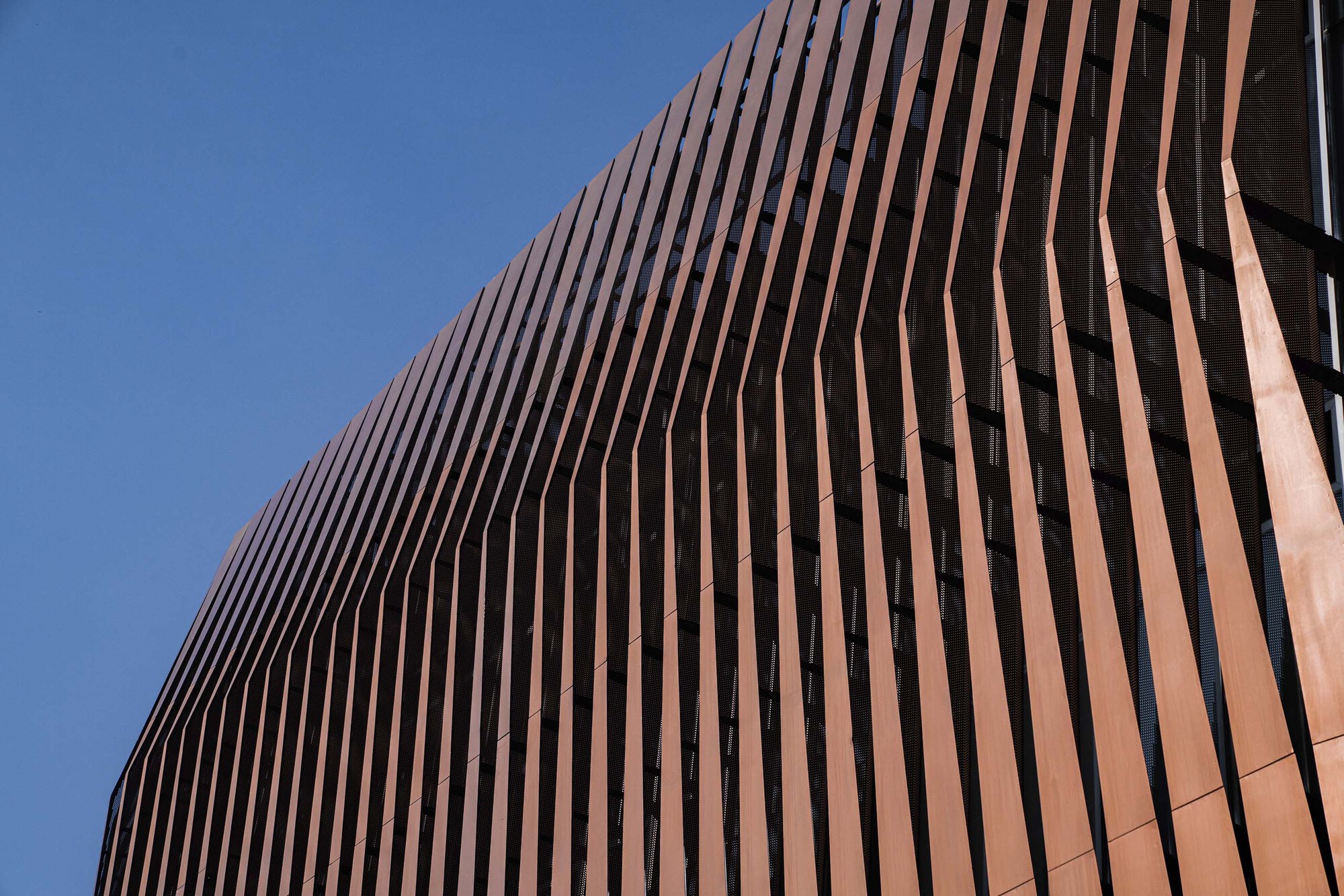 Curved copper-toned vertical fins wrapping the podium facade against clear sky