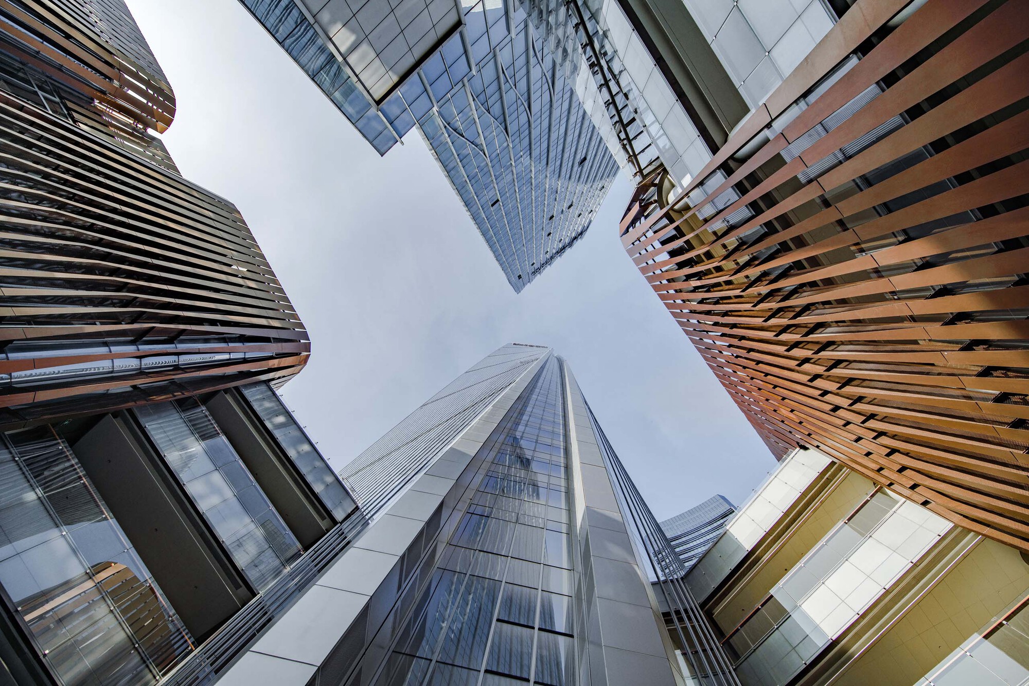 Worm's-eye view of four towers converging around a central courtyard under overcast sky