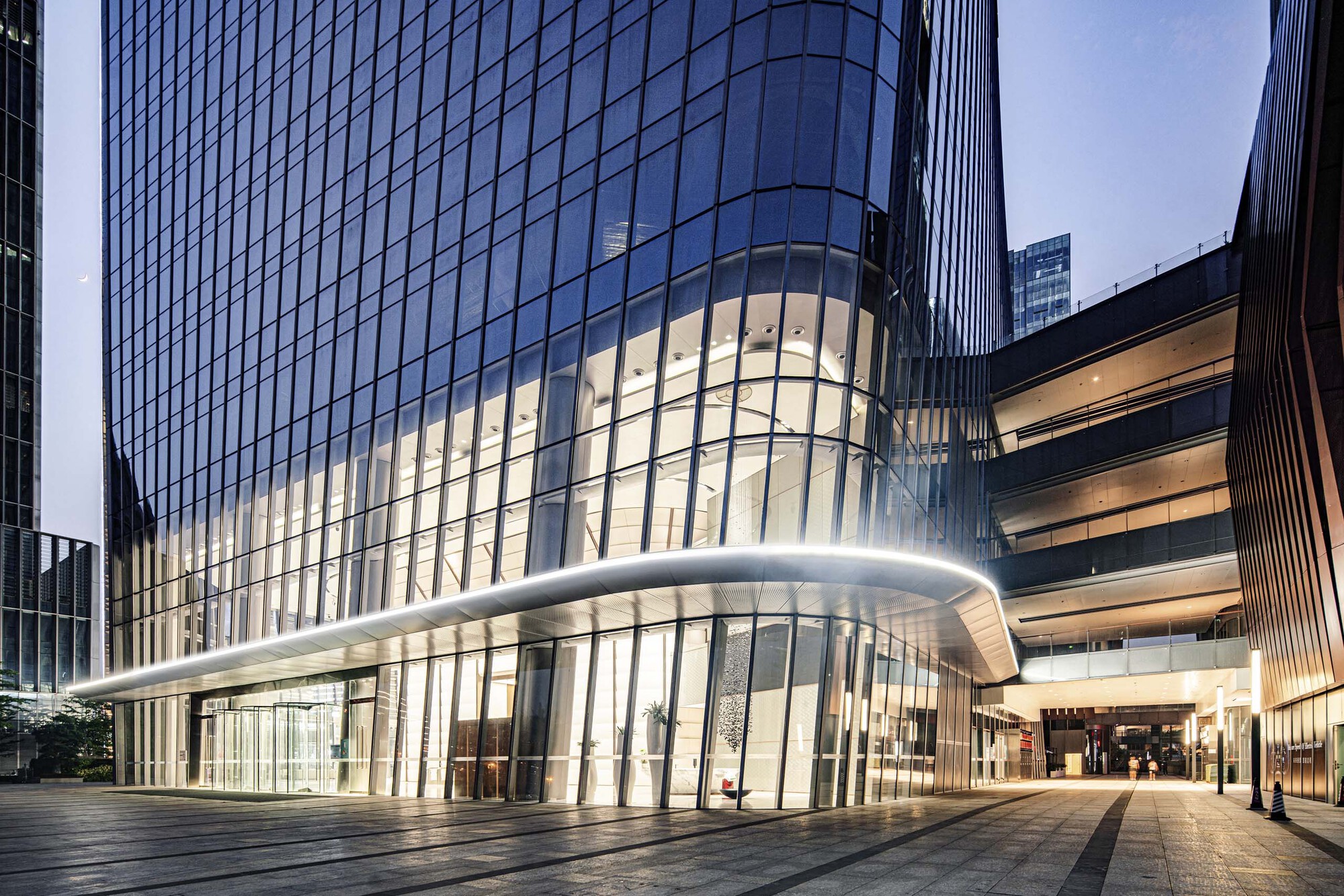 Ground-level entrance with illuminated glass lobby and cantilevered canopy at dusk