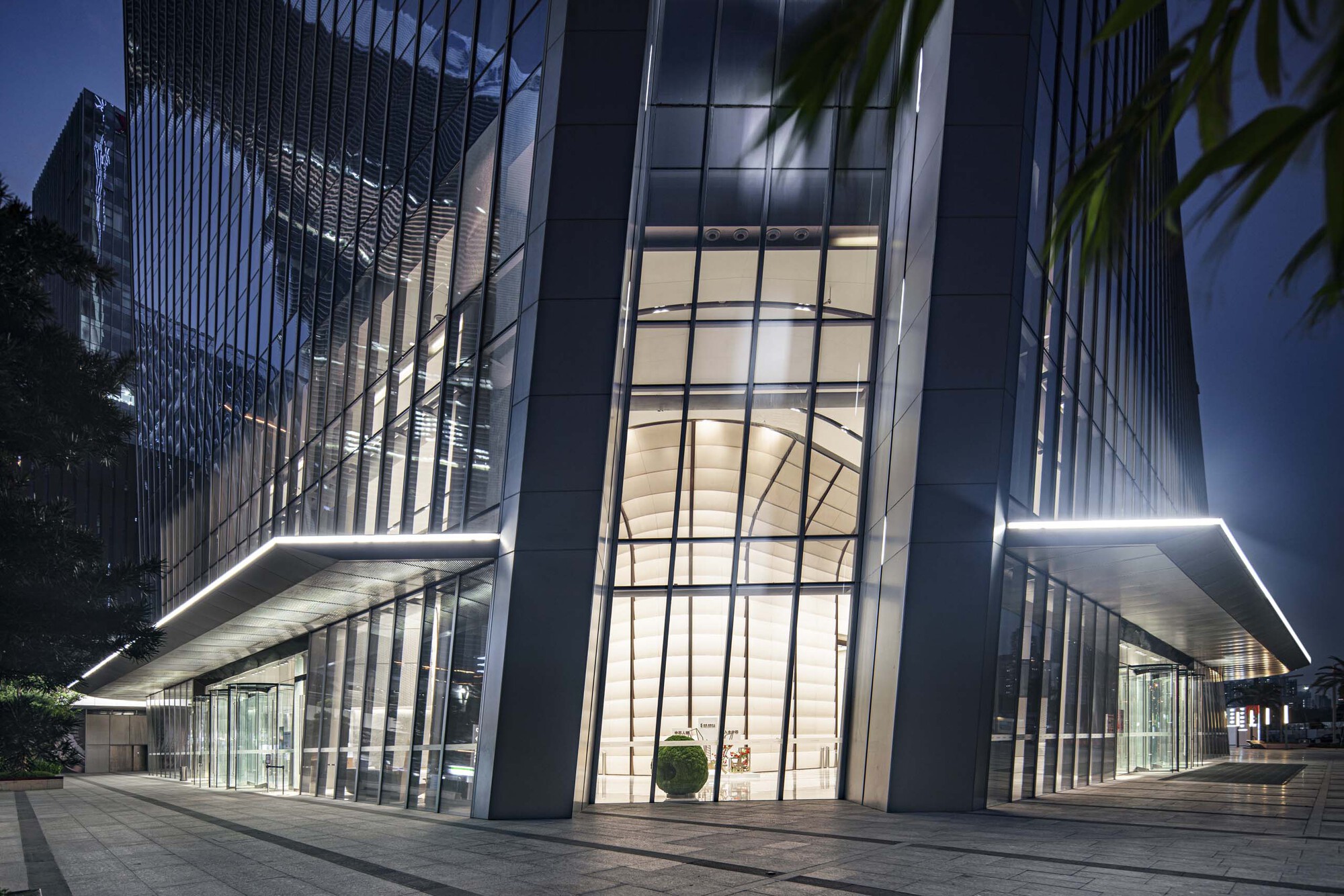 Nighttime view of the illuminated entrance lobby with floating canopy and glass towers above