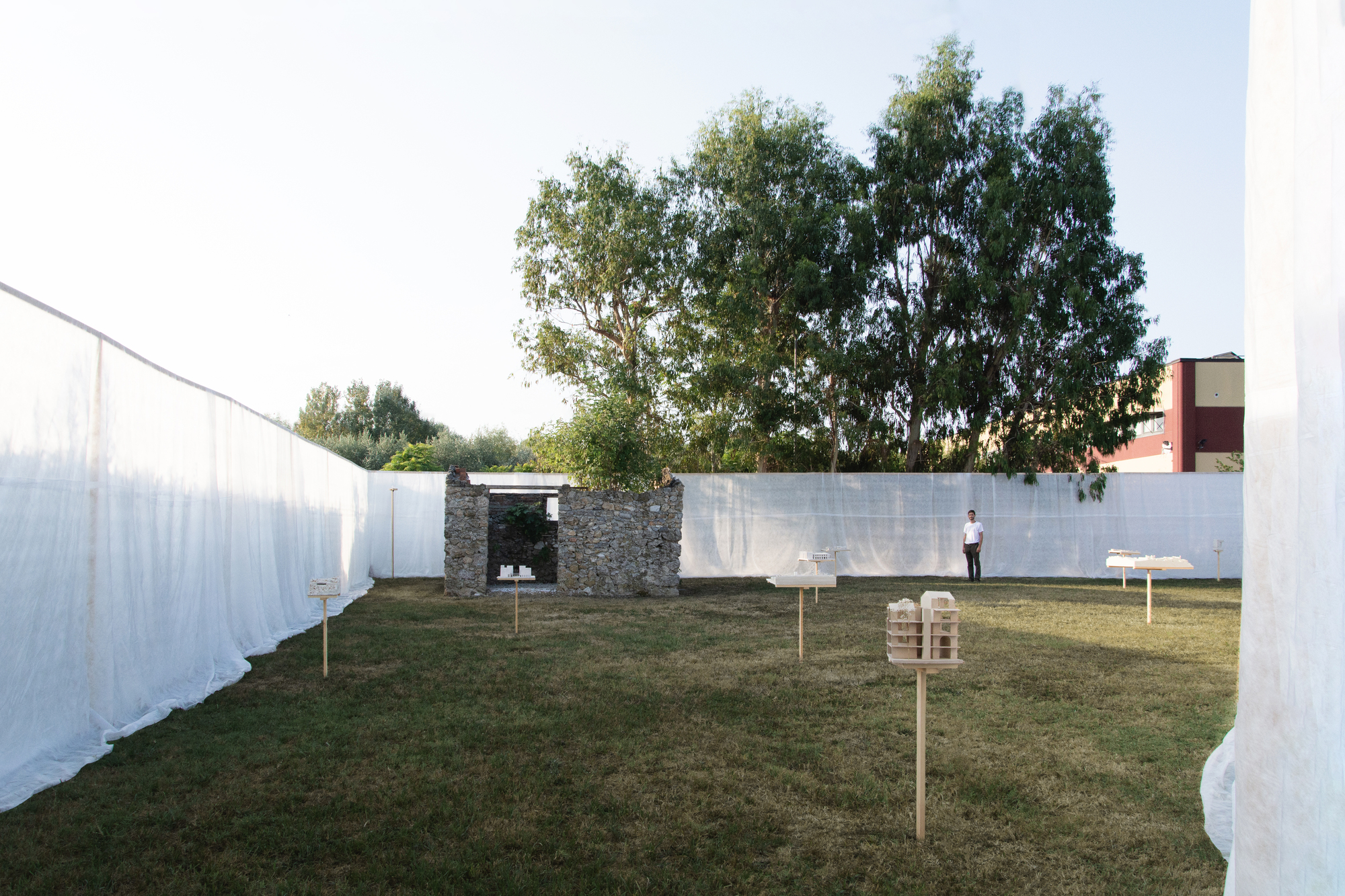 Courtyard with white fabric screens, stone ruin, and a visitor standing on grass at dusk