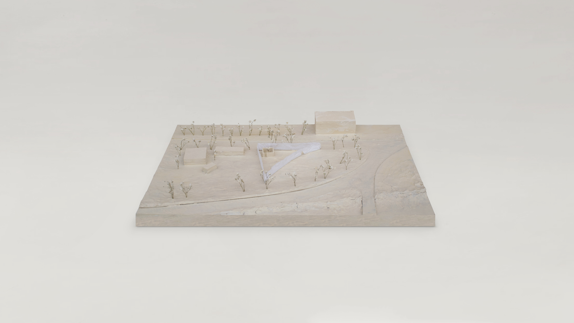 Physical model showing a triangular pavilion in a landscape with miniature trees and pathways