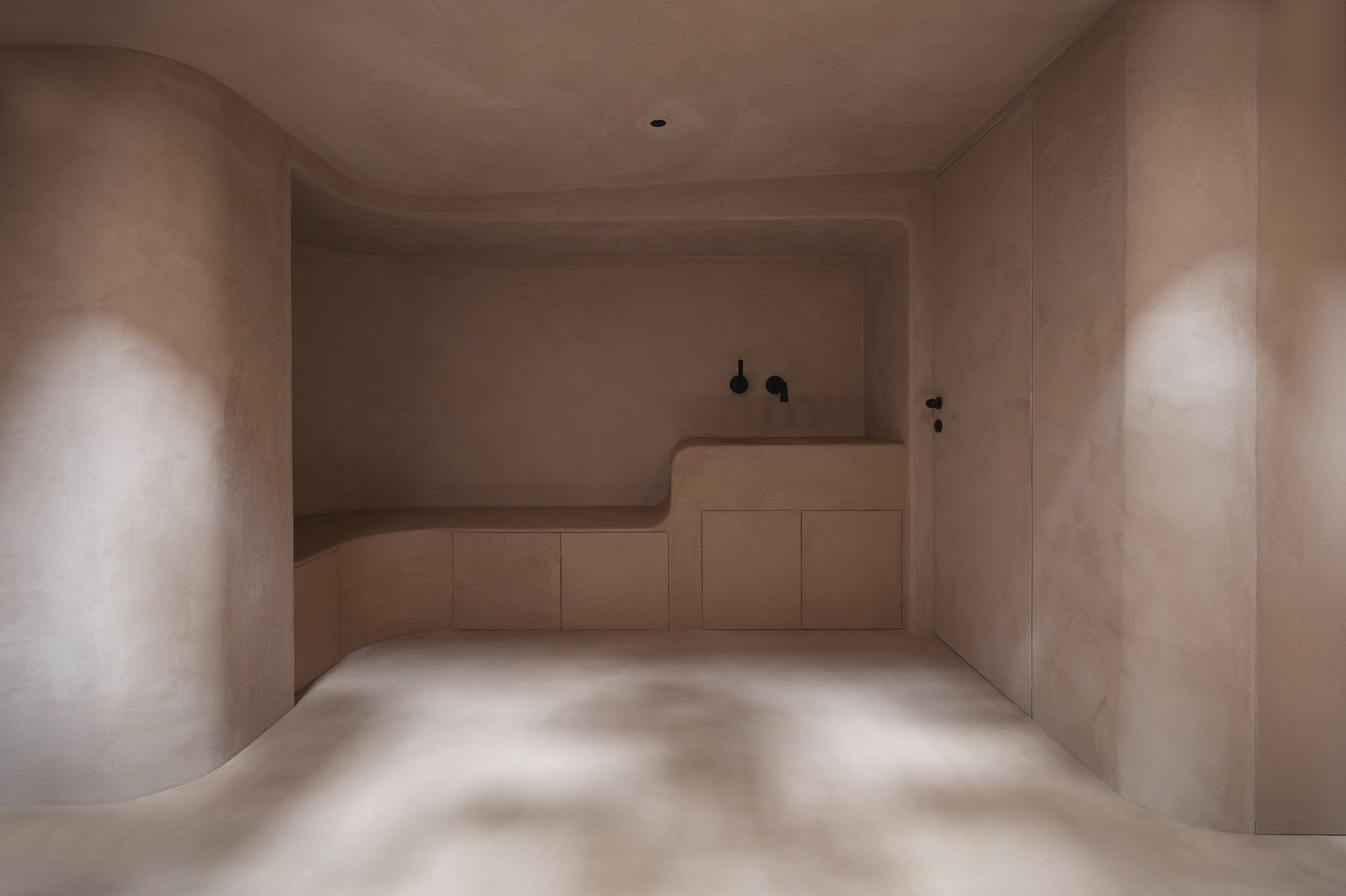 Bathroom with integrated bathtub and vanity in pale plastered walls with soft daylight from above