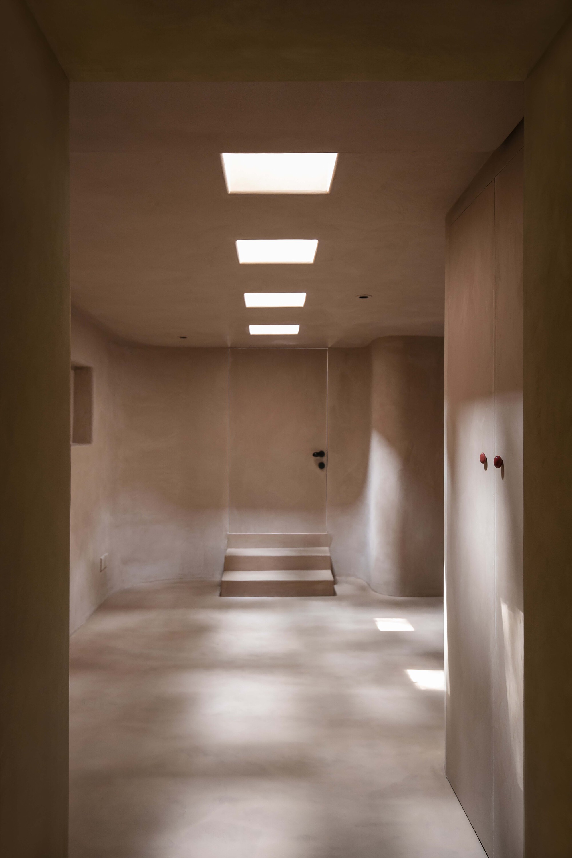 Corridor with four recessed ceiling lights illuminating plastered walls and a stepped threshold ahead
