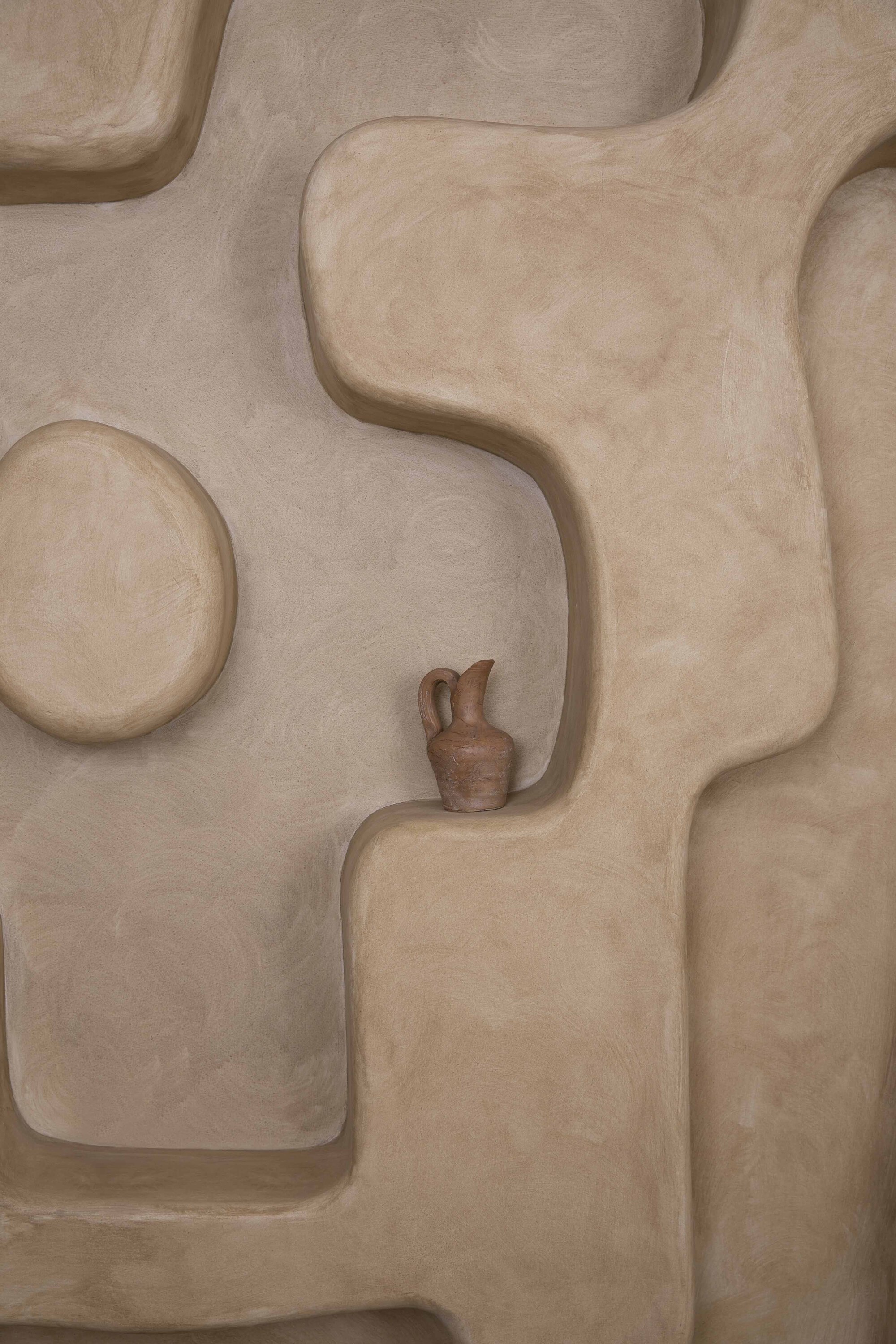 Close-up of plastered wall shelving with organic curved niches holding a ceramic vessel
