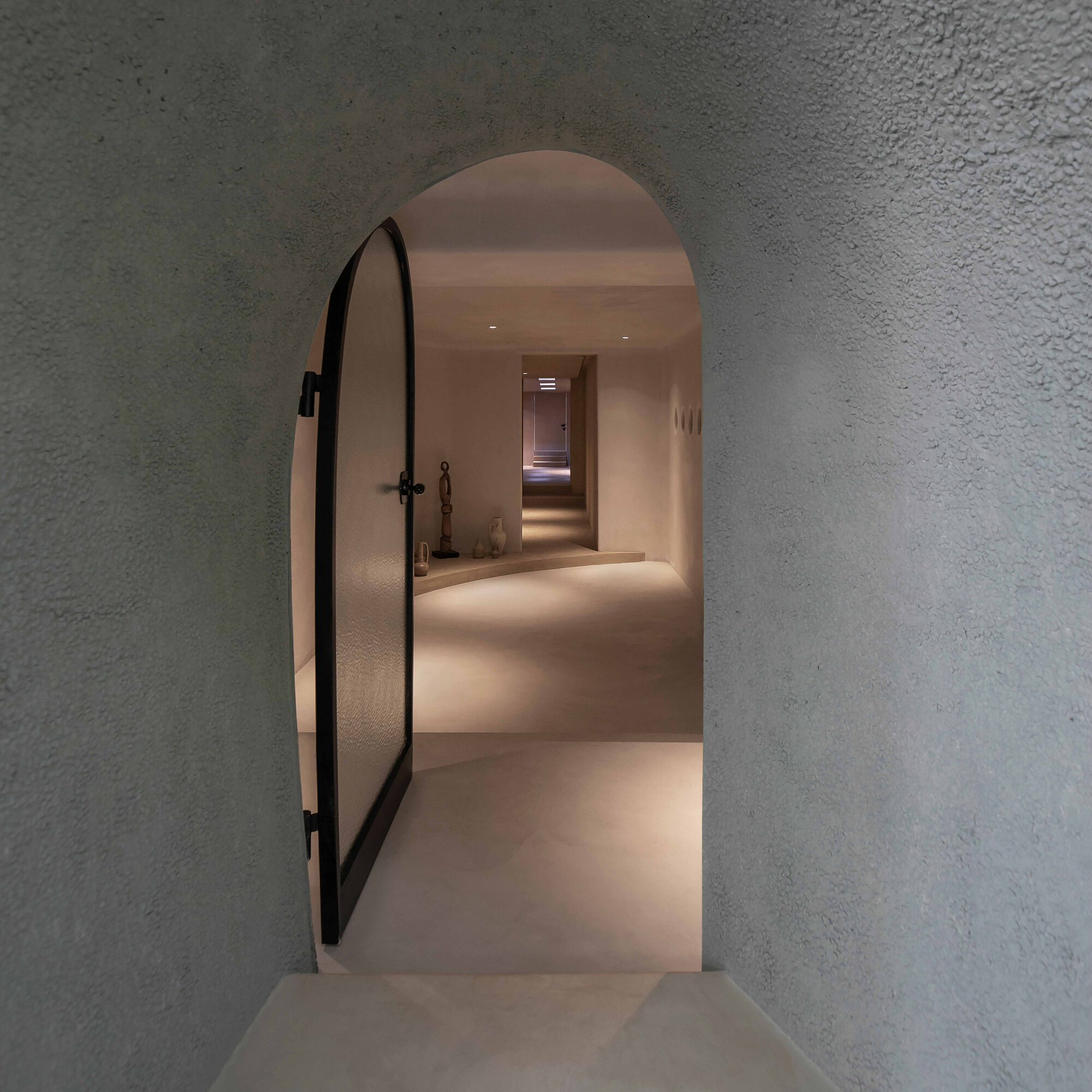 Arched doorway with black metal door frame opening onto a plastered hallway with embedded lighting