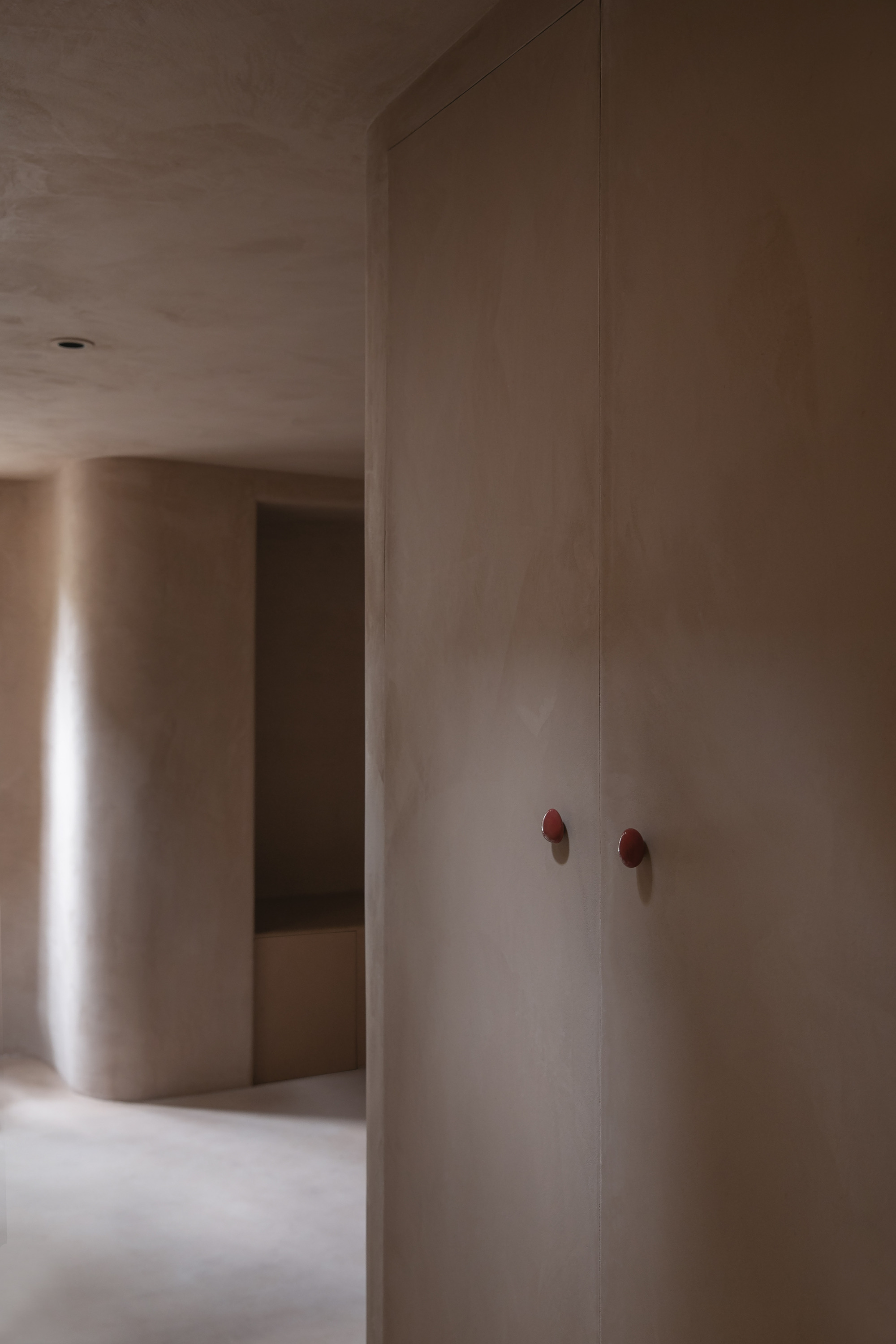 Plastered wall panels with bronze hardware at a corner threshold between two softly lit rooms