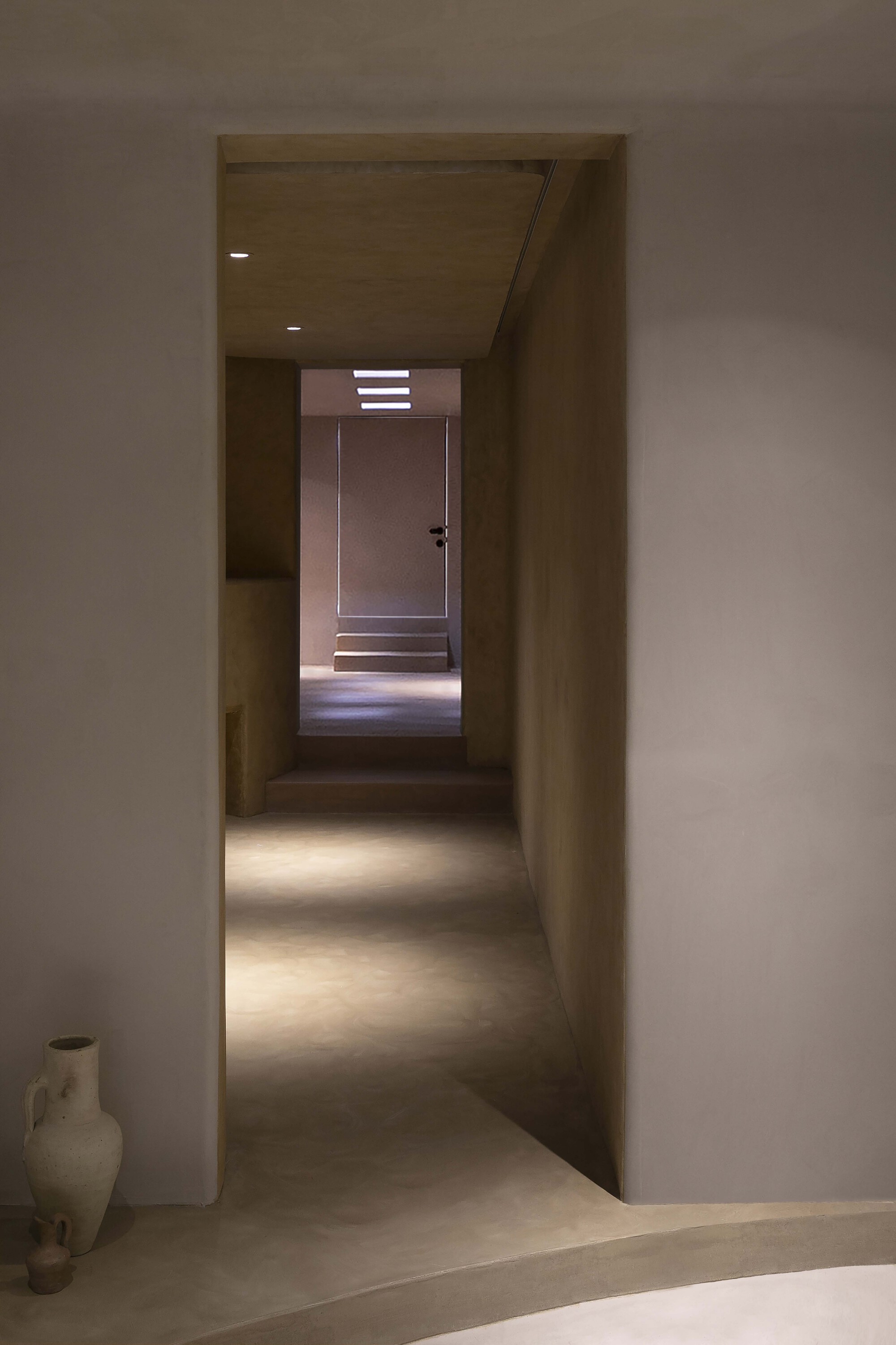 Sequence of thresholds leading to a backlit door at the end of a long corridor
