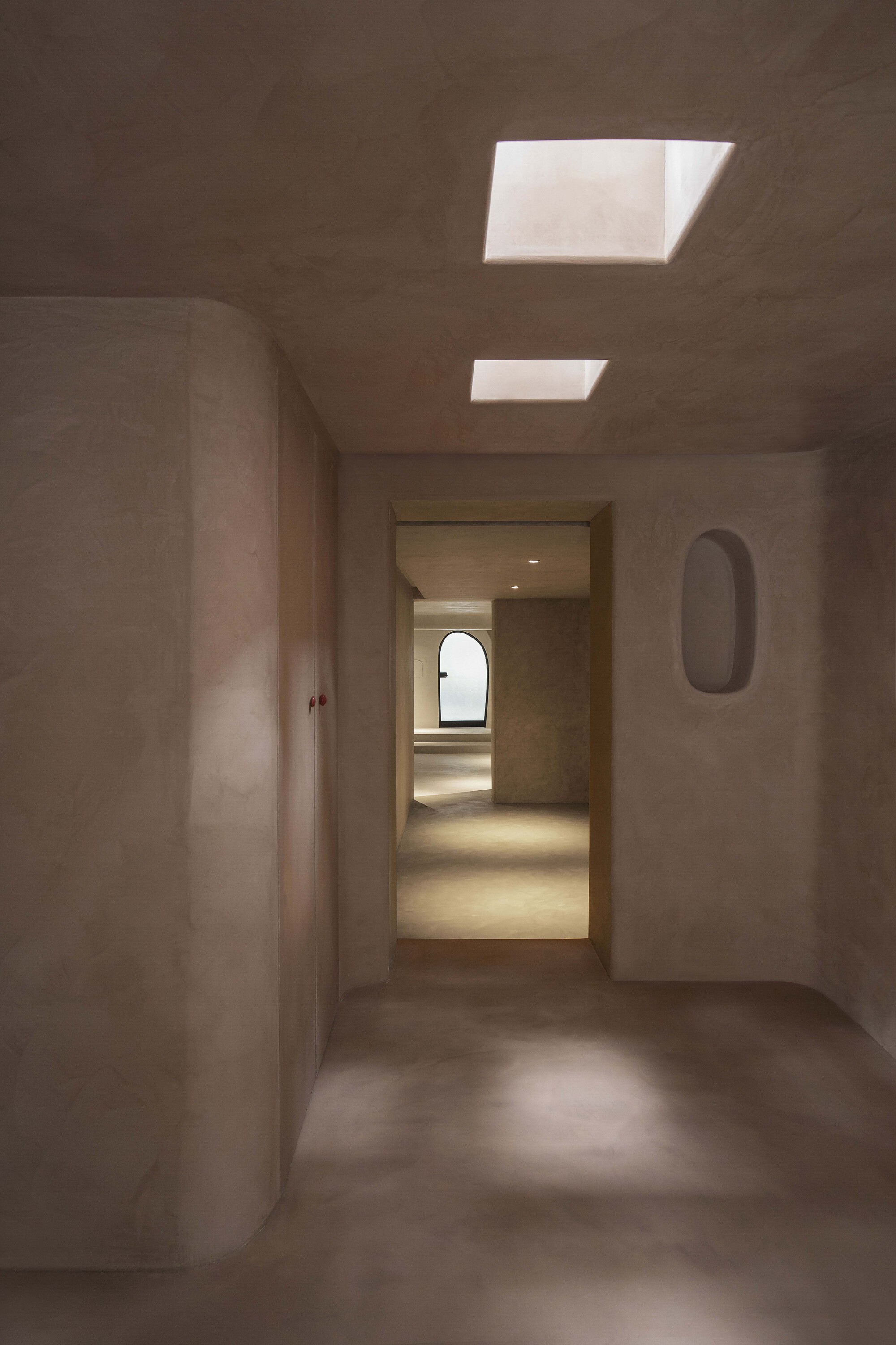 Plastered room with rectangular skylights and doorway framing a view through multiple chambers