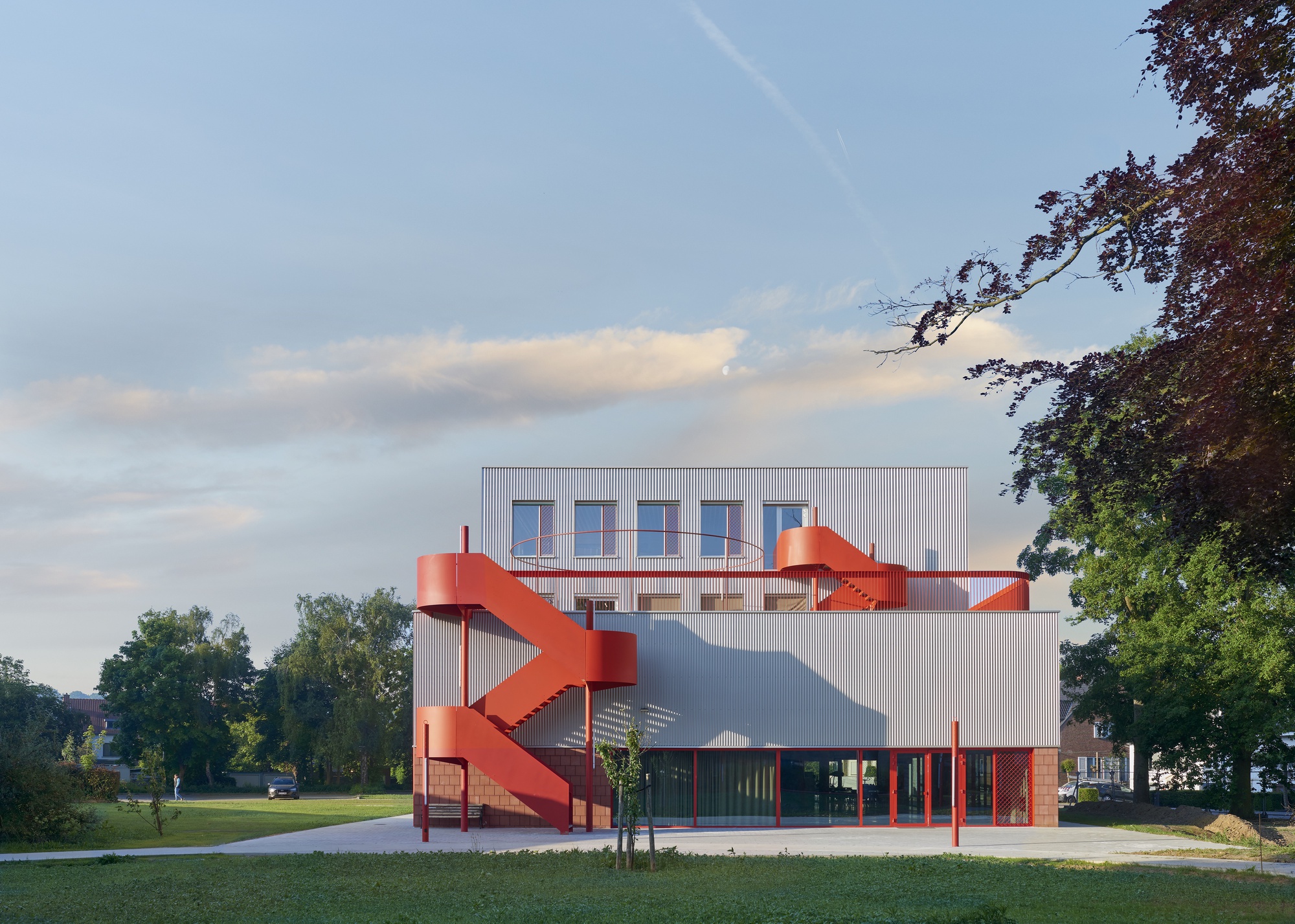View of the building with red exterior staircase and corrugated metal cladding across a green lawn at dusk