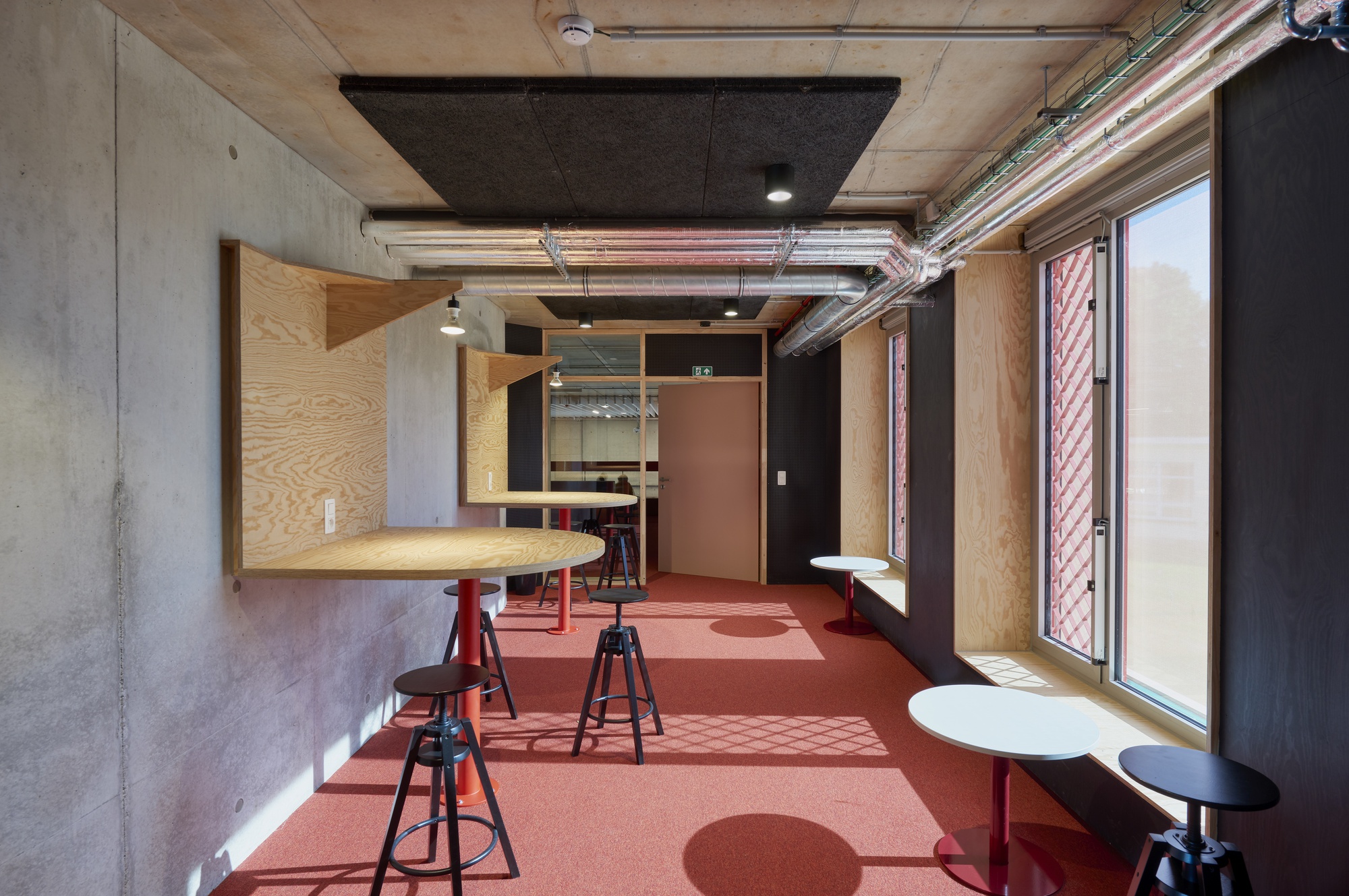 Interior workspace with plywood casework, concrete ceiling, terracotta flooring, and exposed conduit near a window