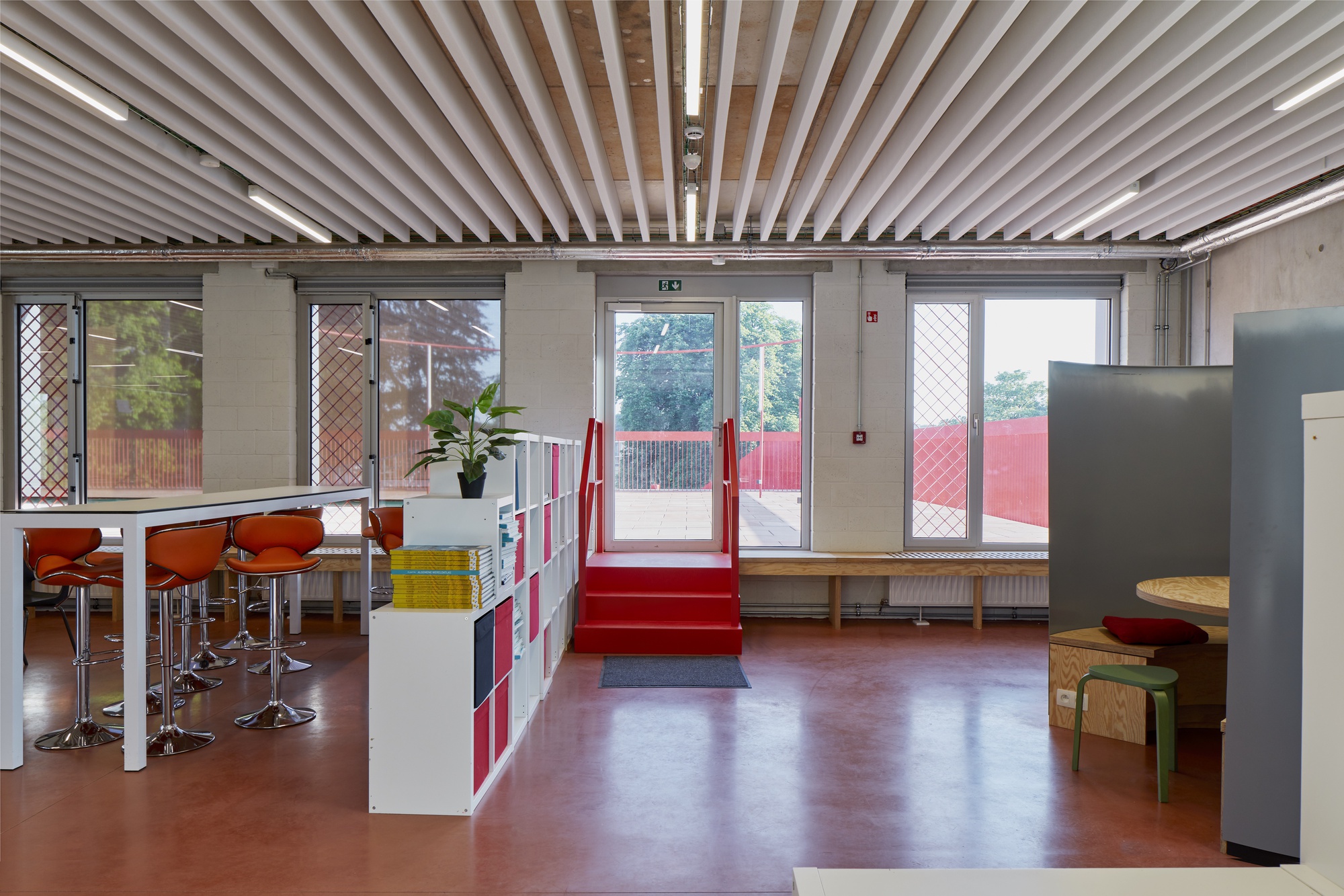 Open interior with linear baffle ceiling, red rubber flooring, and glass doors leading to an exterior terrace