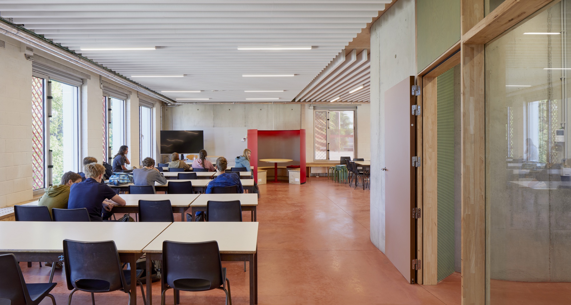 Meeting room with occupants at tables under timber and white acoustic ceiling panels with daylight from left