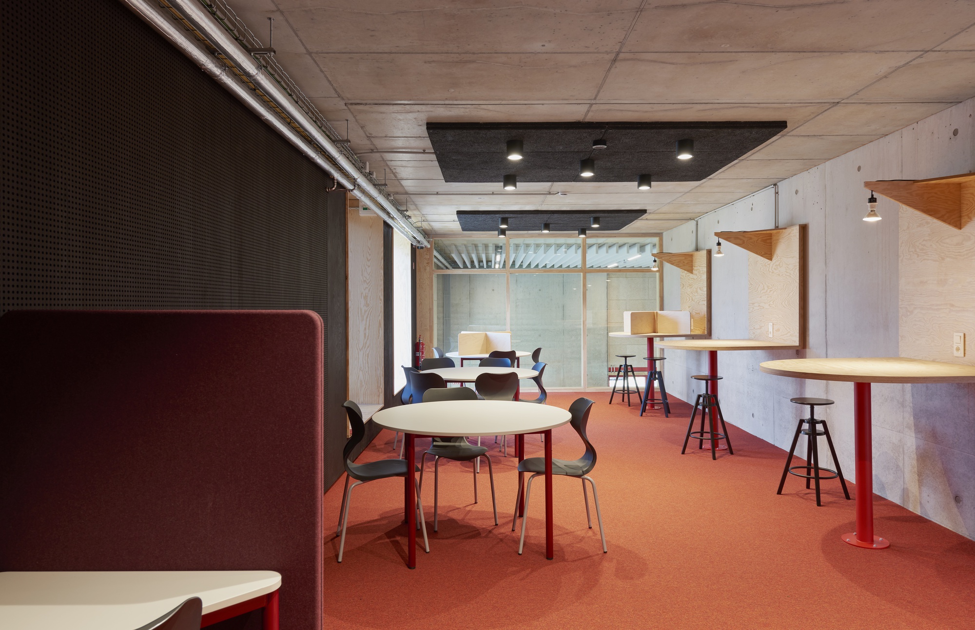 Casual seating area with terracotta flooring, perforated acoustic wall panels, and timber-framed glass partitions beyond