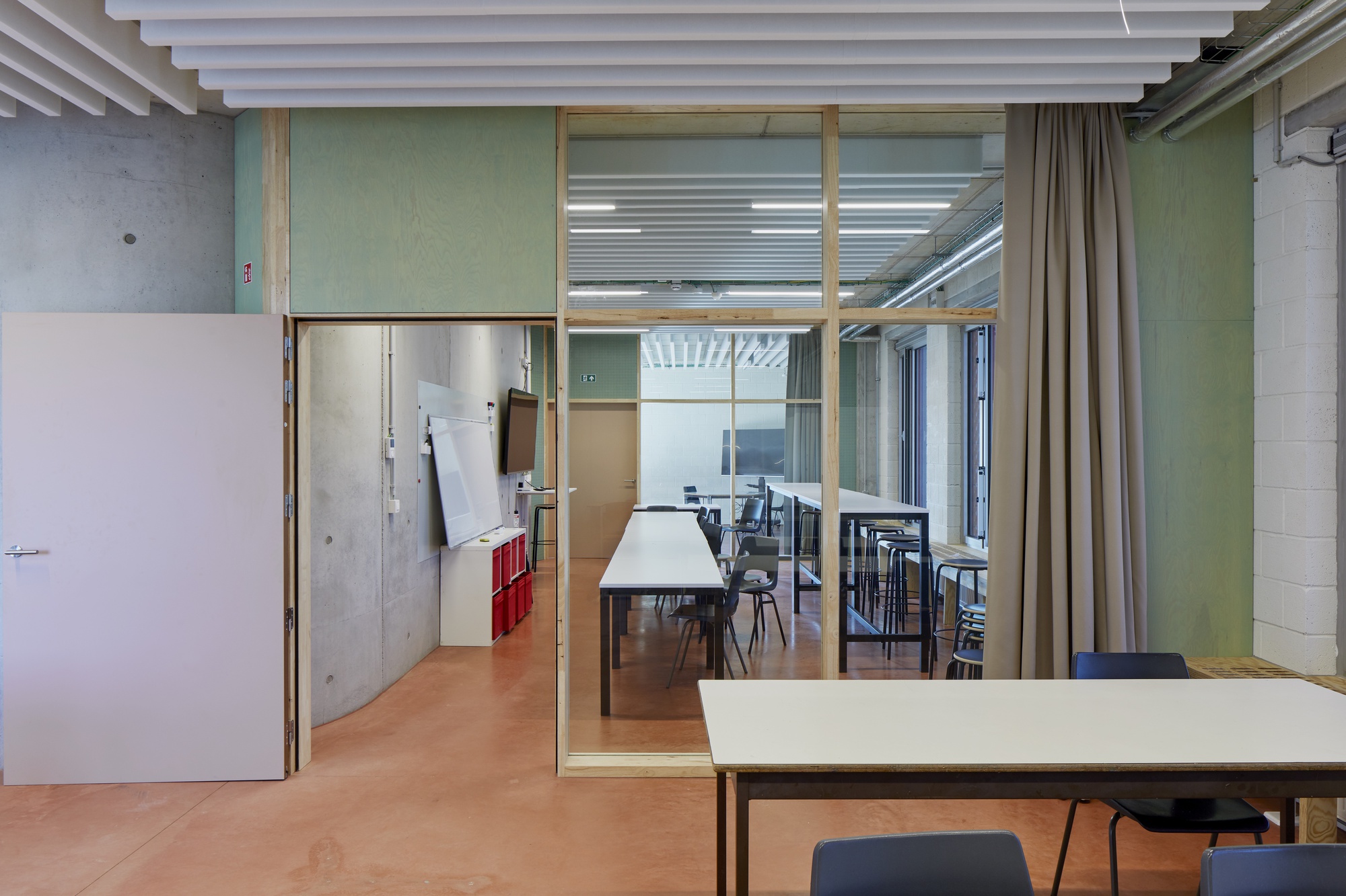 Glass-enclosed meeting room with timber frame visible through adjacent work space with beige flooring and curtain dividers