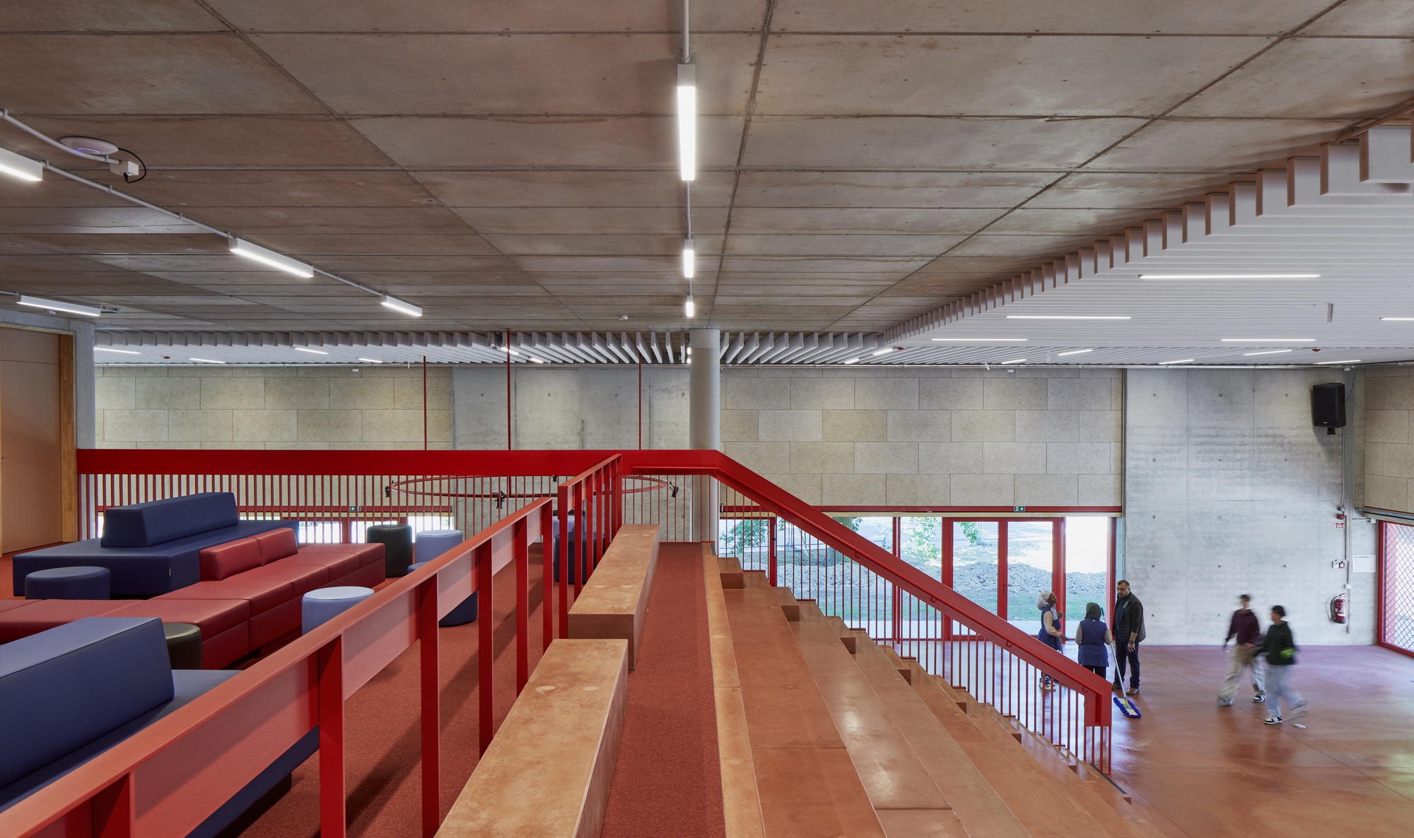 Upper level mezzanine with red steel railing, cork flooring, and figures moving through the entry hall below