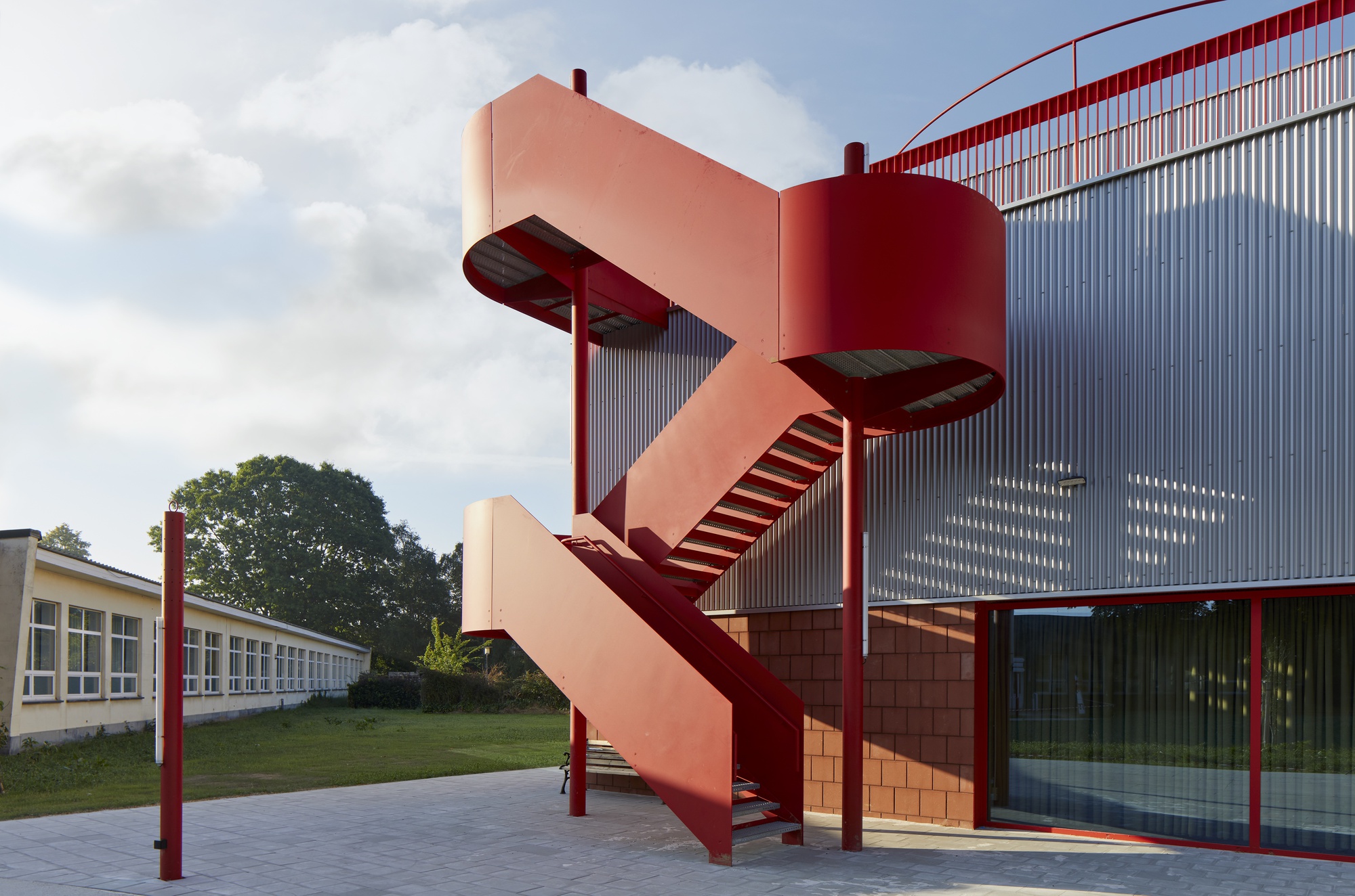 Exterior view of the salmon-pink spiral fire escape stair wrapping around red steel columns on a cloudy day