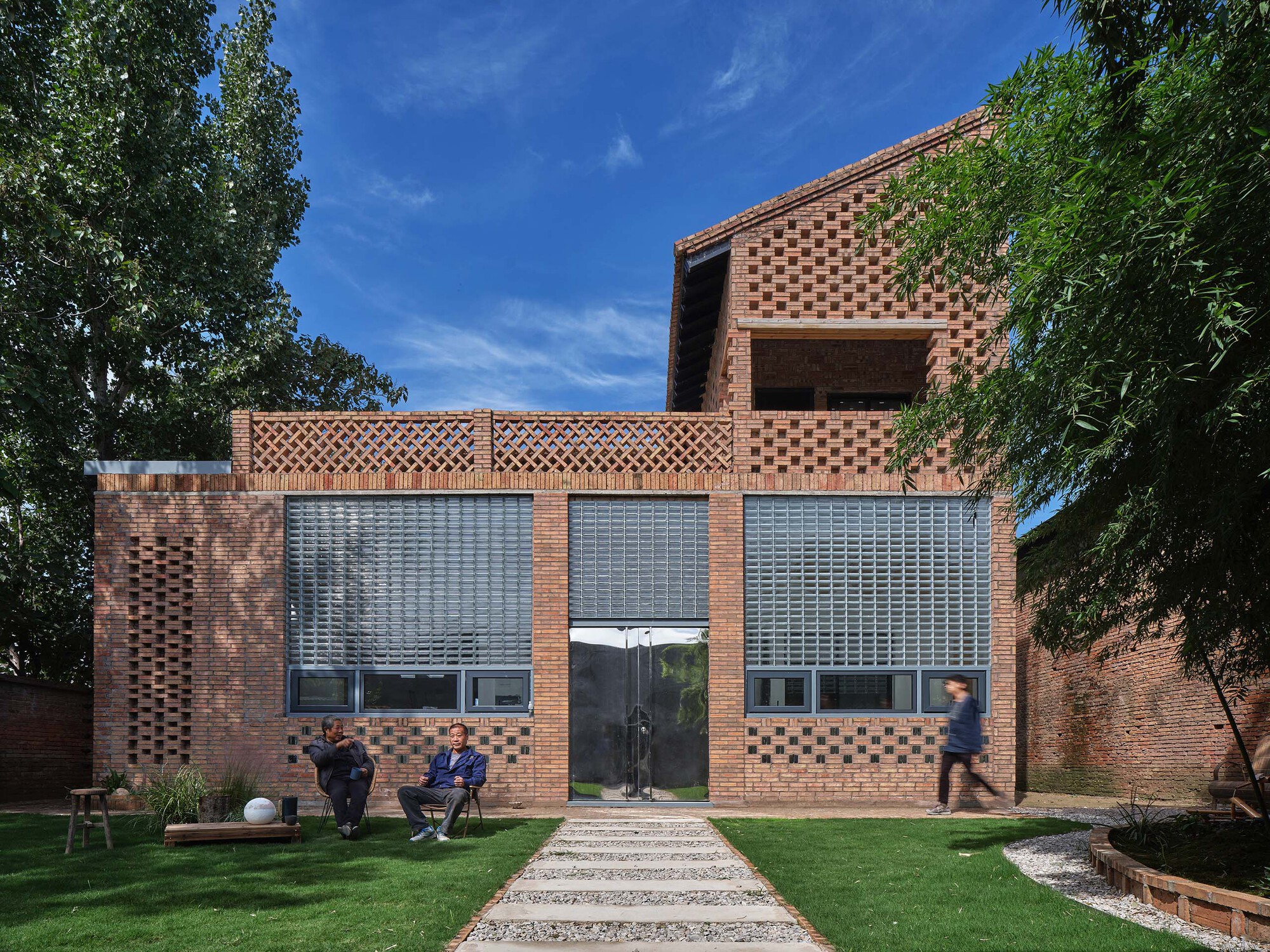 Facade with patterned brick screening and glass block windows framed by mature trees and a lawn